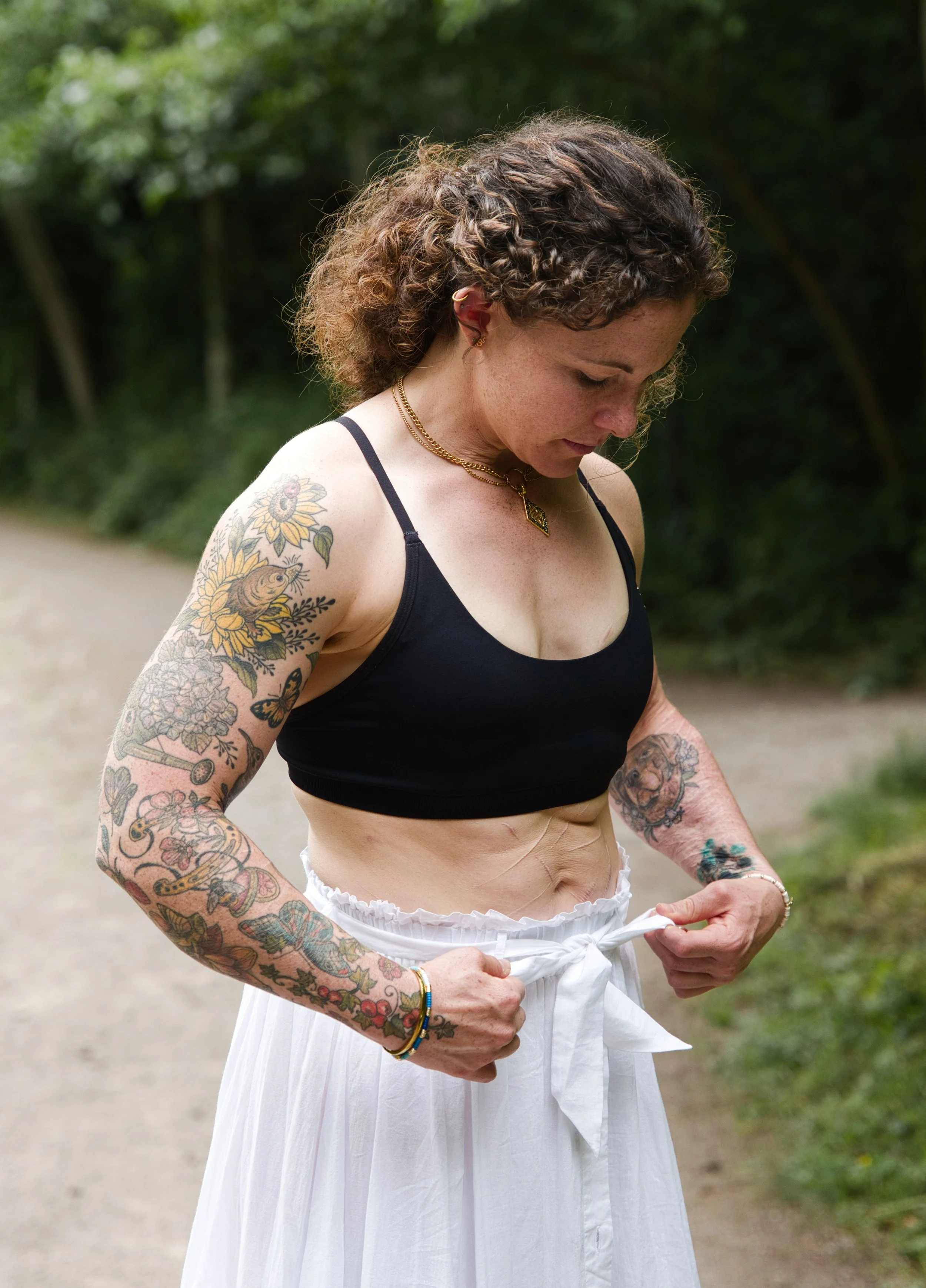 Woman adjusting a white skirt during an outdoor portrait session in Gloucestershire, showing tattoos, strength and personal character.