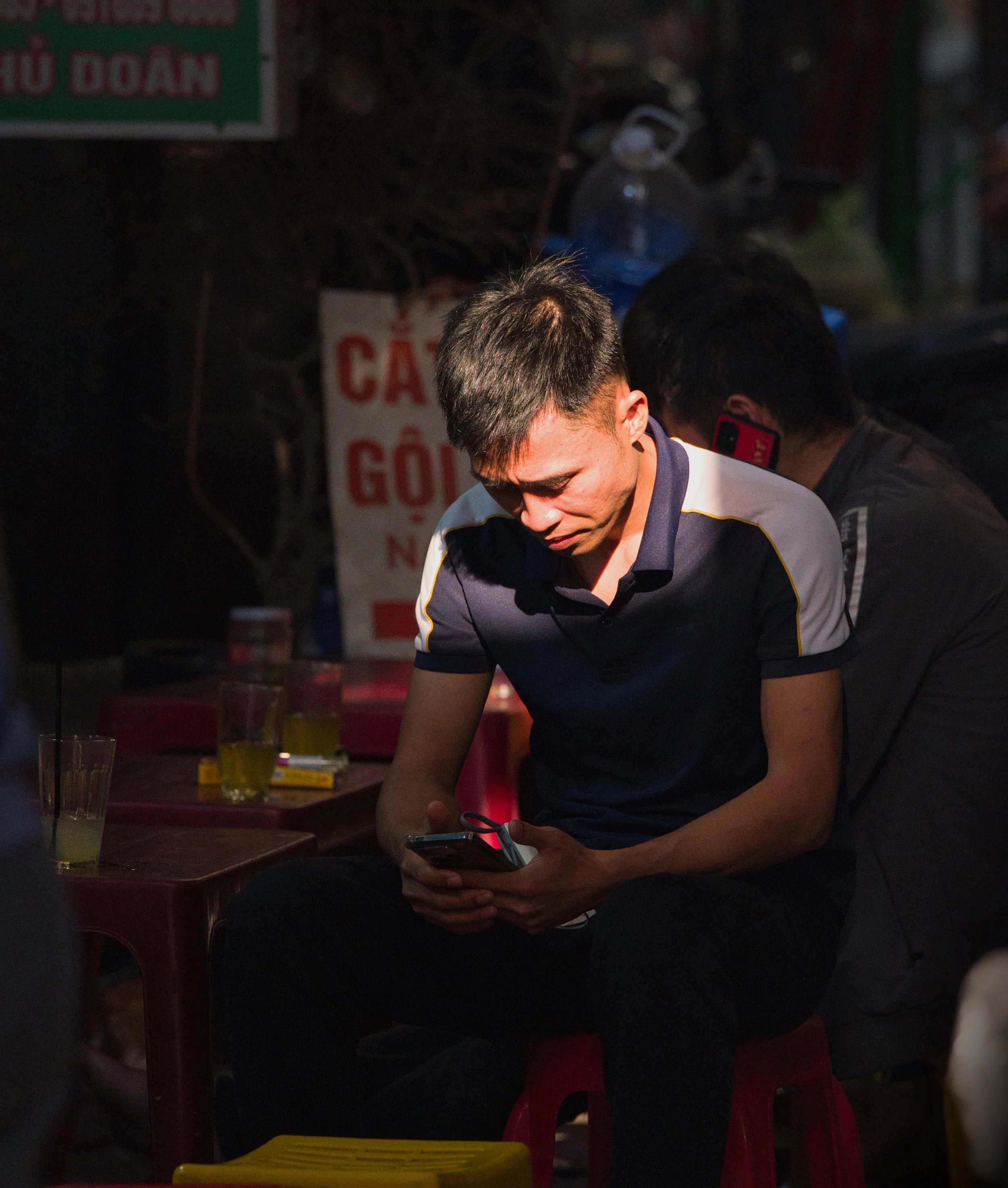 Portrait of a man illuminated by harsh evening light while looking at his phone in Hanoi