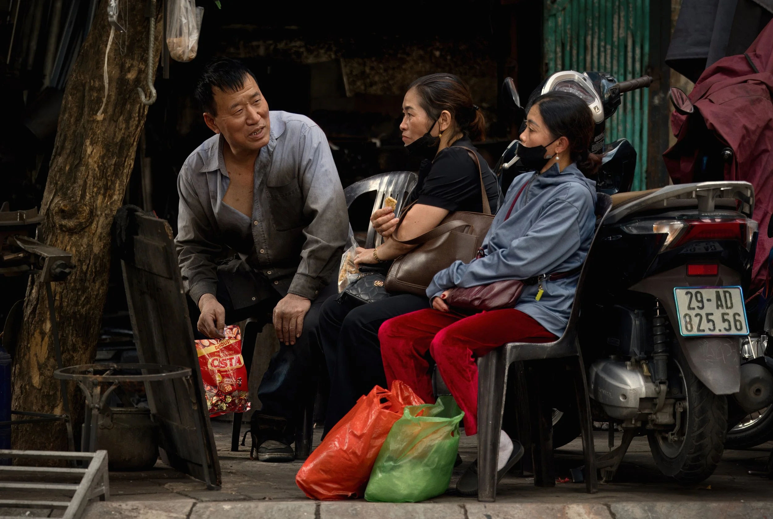 Candid street scene of three people talking beside a scooter in Hanoi
