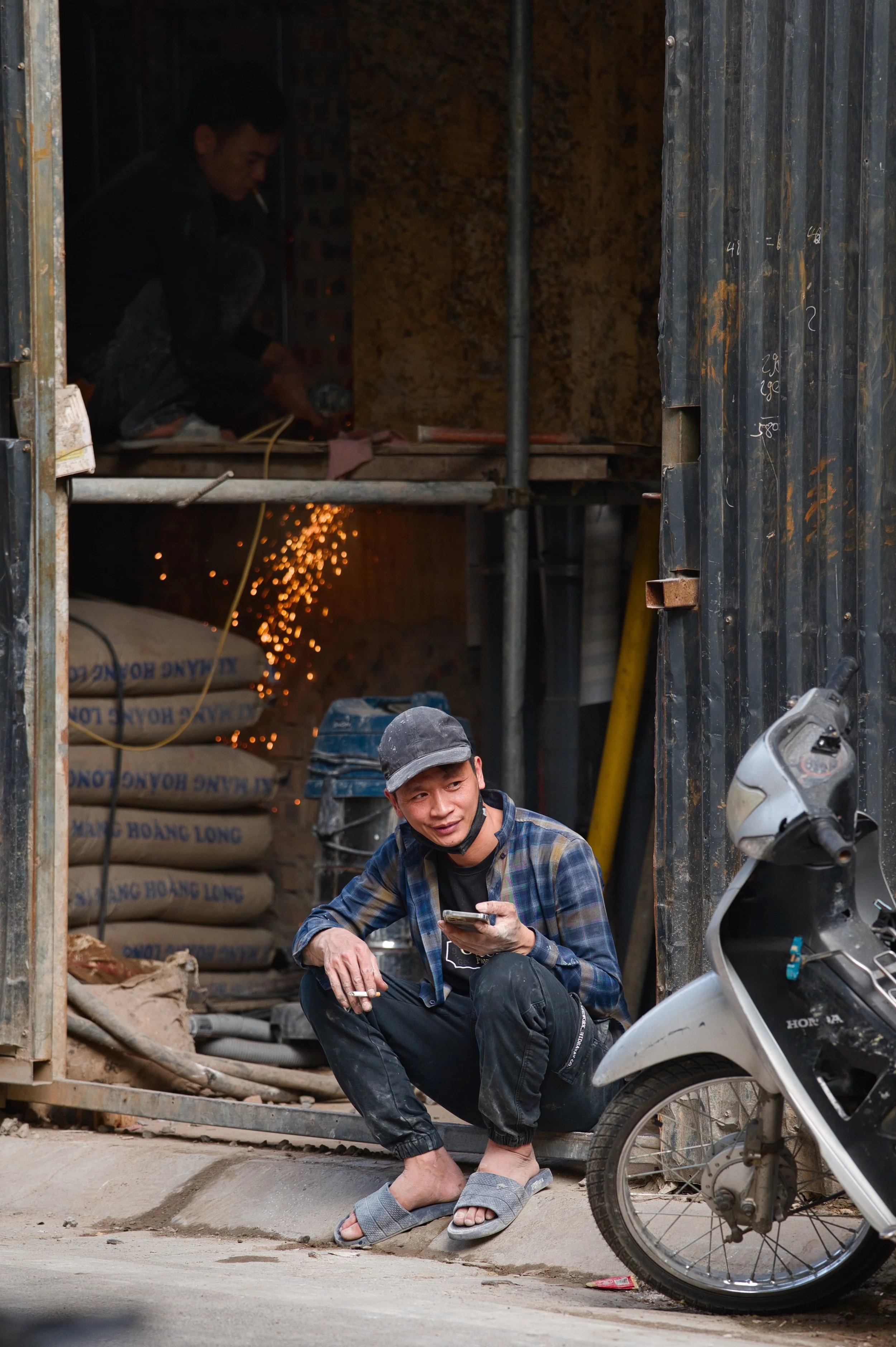 Street portrait of a man sitting outside a workshop in Hanoi with sparks glowing in the background