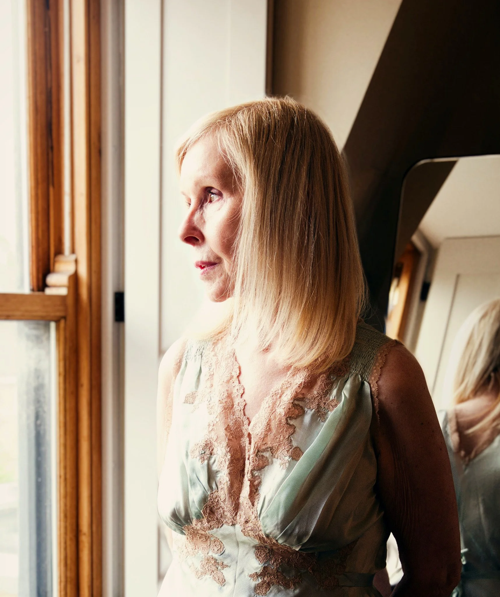 Woman in delicate sage-green lace lingerie gazing thoughtfully through a window, illuminated by soft natural light in an intimate boudoir portrait.