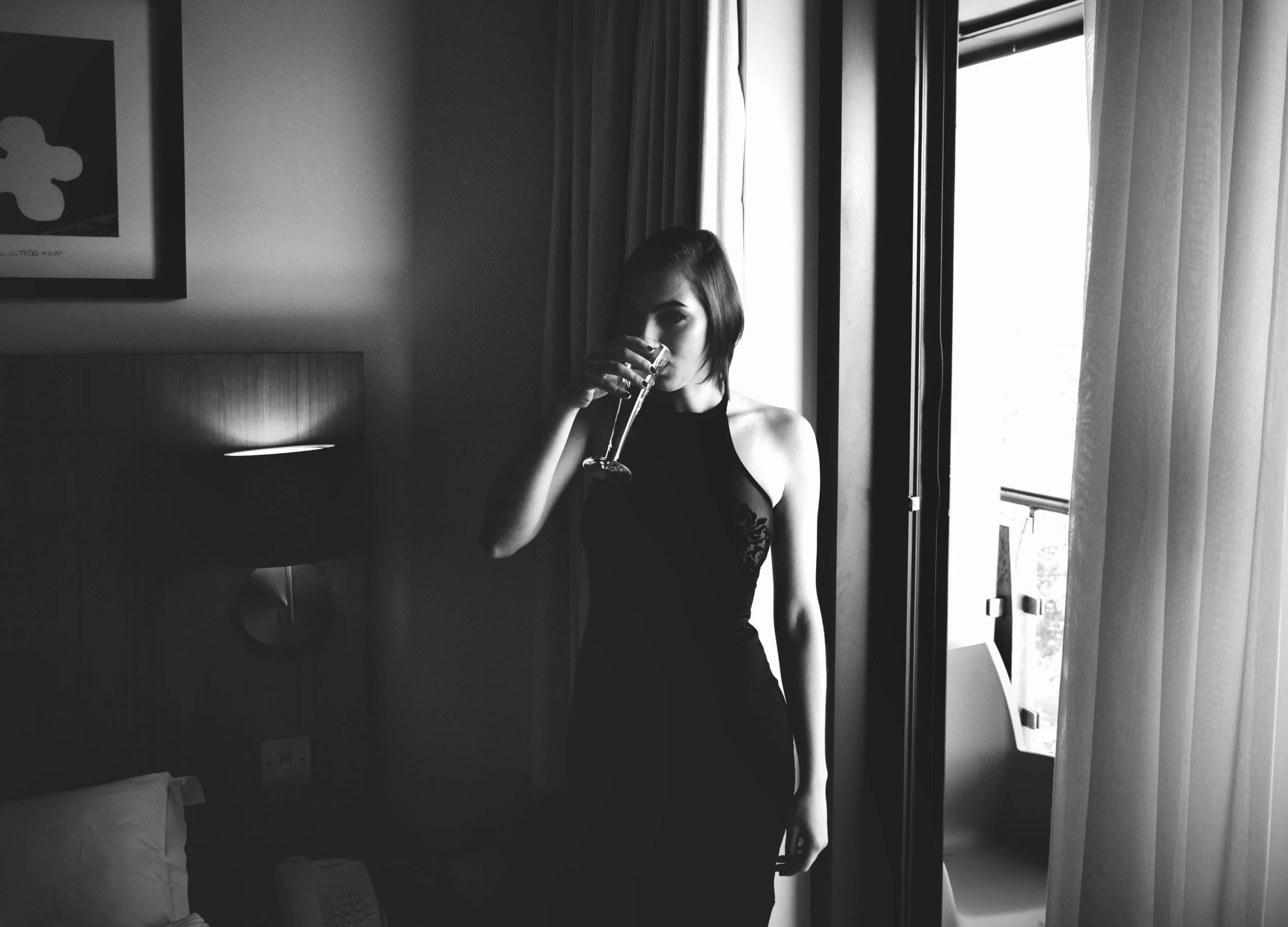 Black and white portrait of a woman standing beside a window in dramatic light