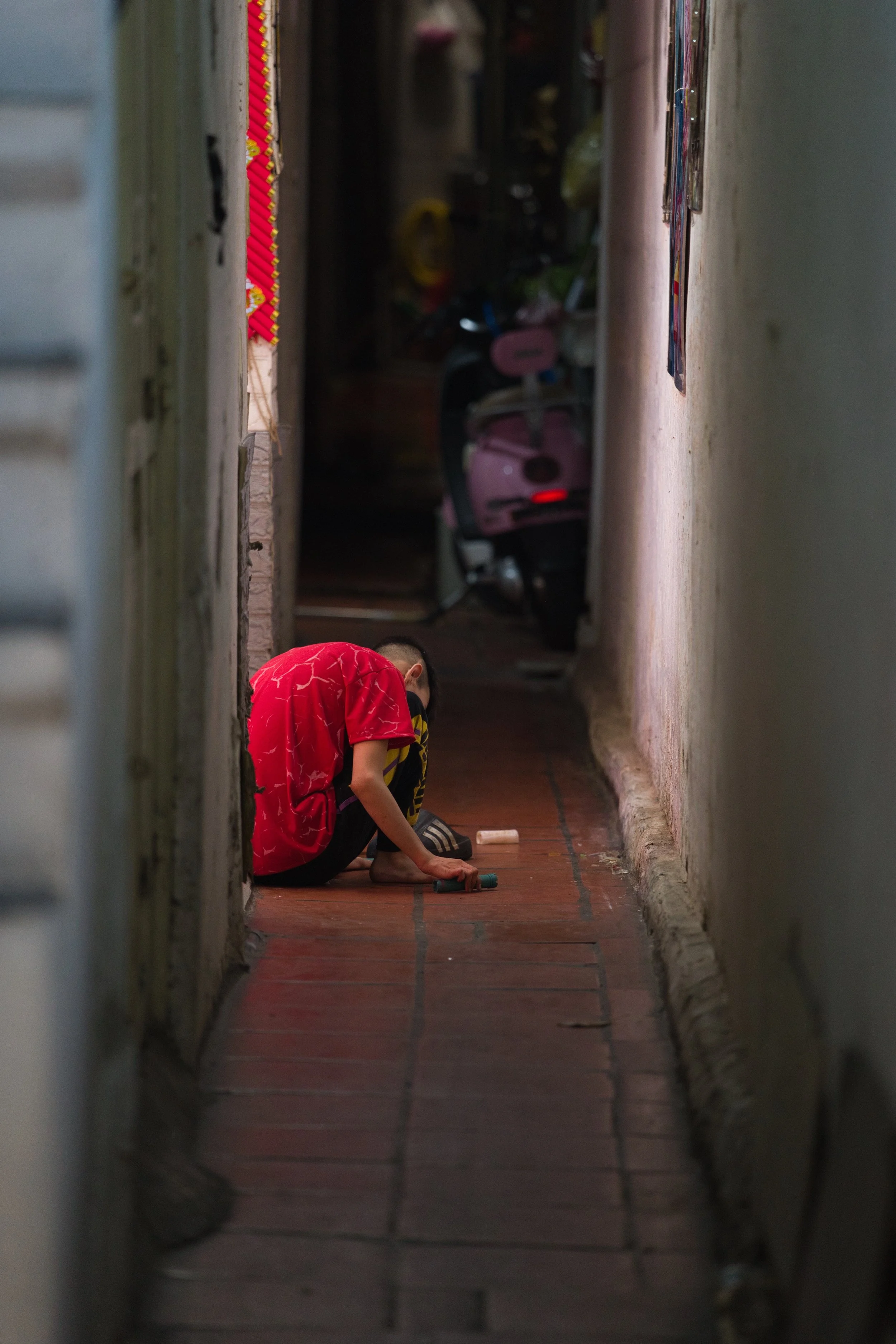 Child sitting in a narrow Hanoi alleyway illuminated by soft natural light