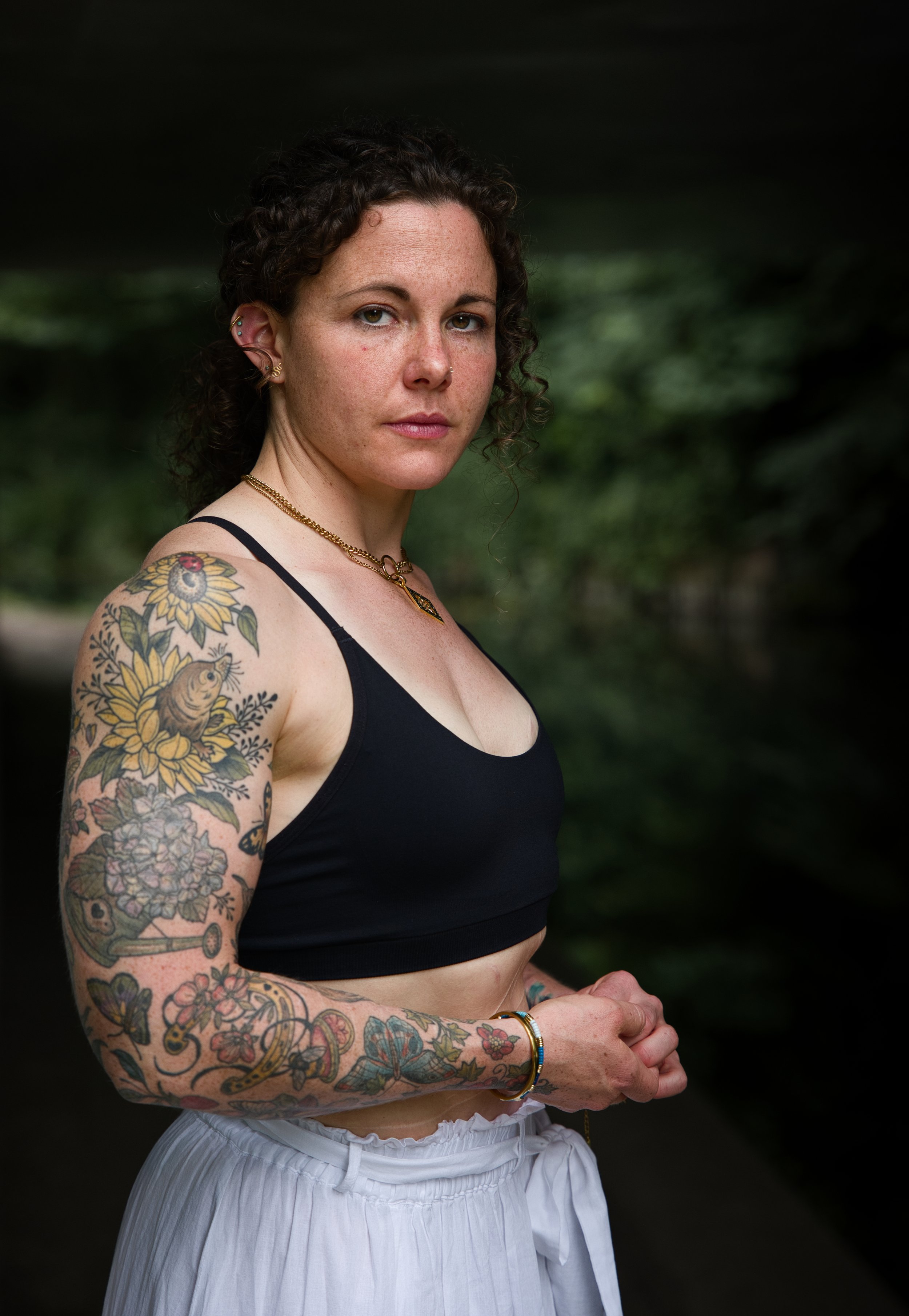 Environmental portrait of a tattooed woman beside a canal in Gloucestershire, photographed in natural light beneath an underpass.