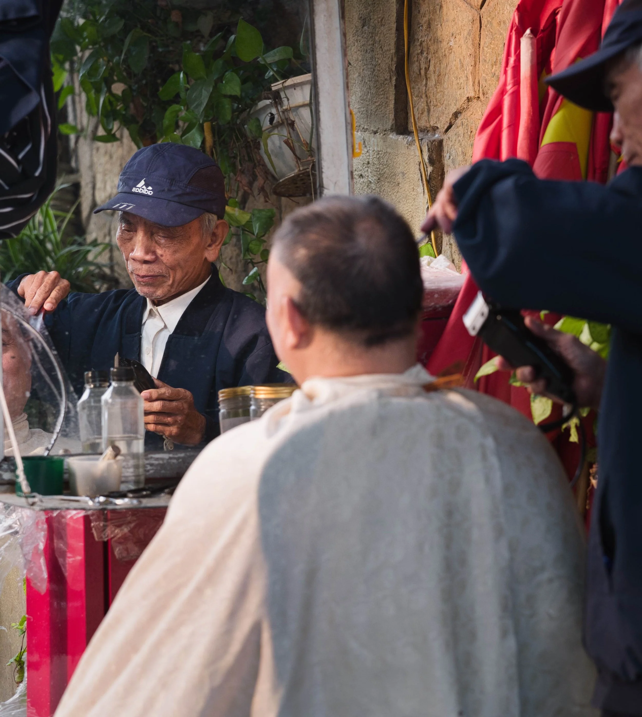 Street barber cutting a customer’s hair in Hanoi while another man waits nearby holding clippers