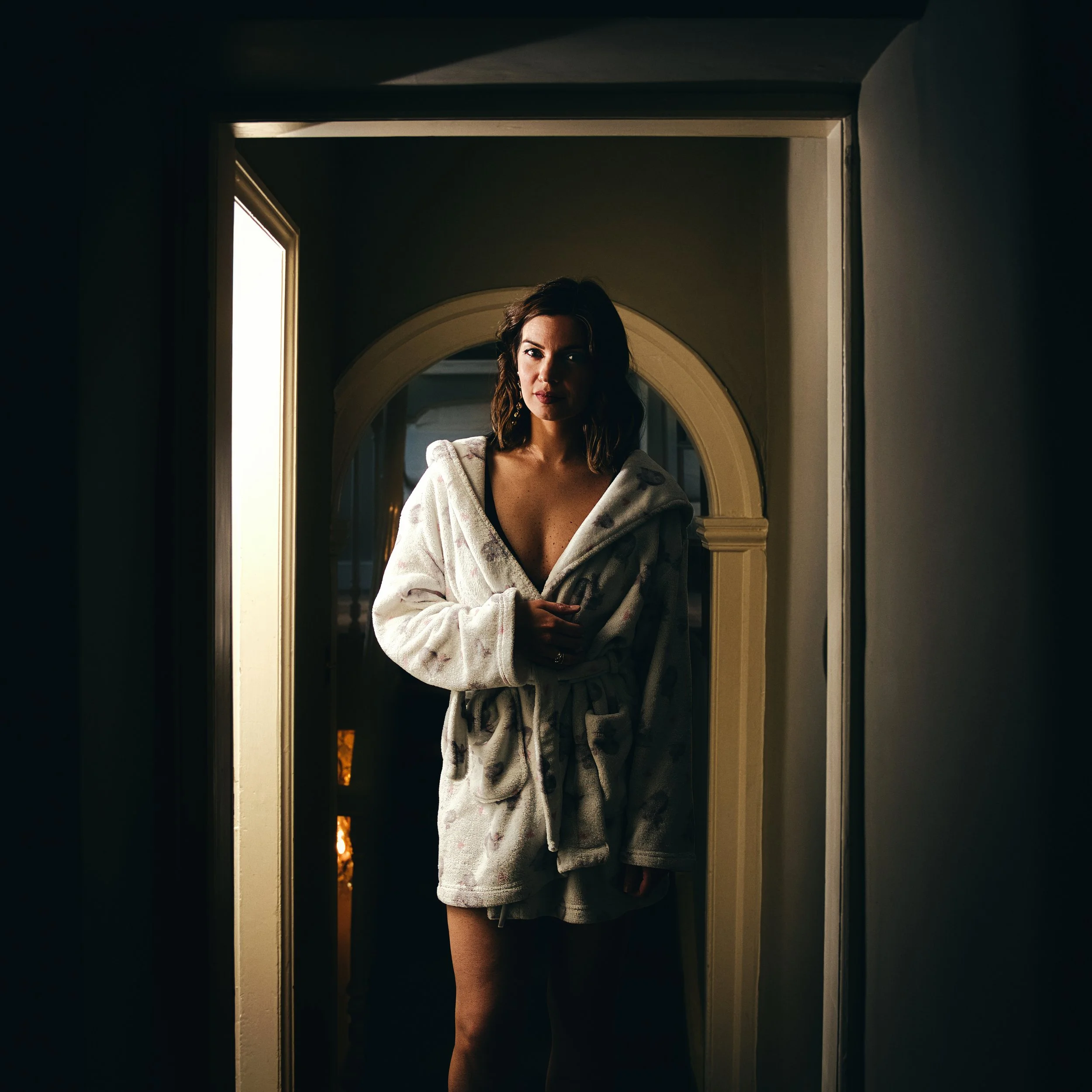 Cinematic boudoir portrait of a woman standing in a doorway wearing a robe