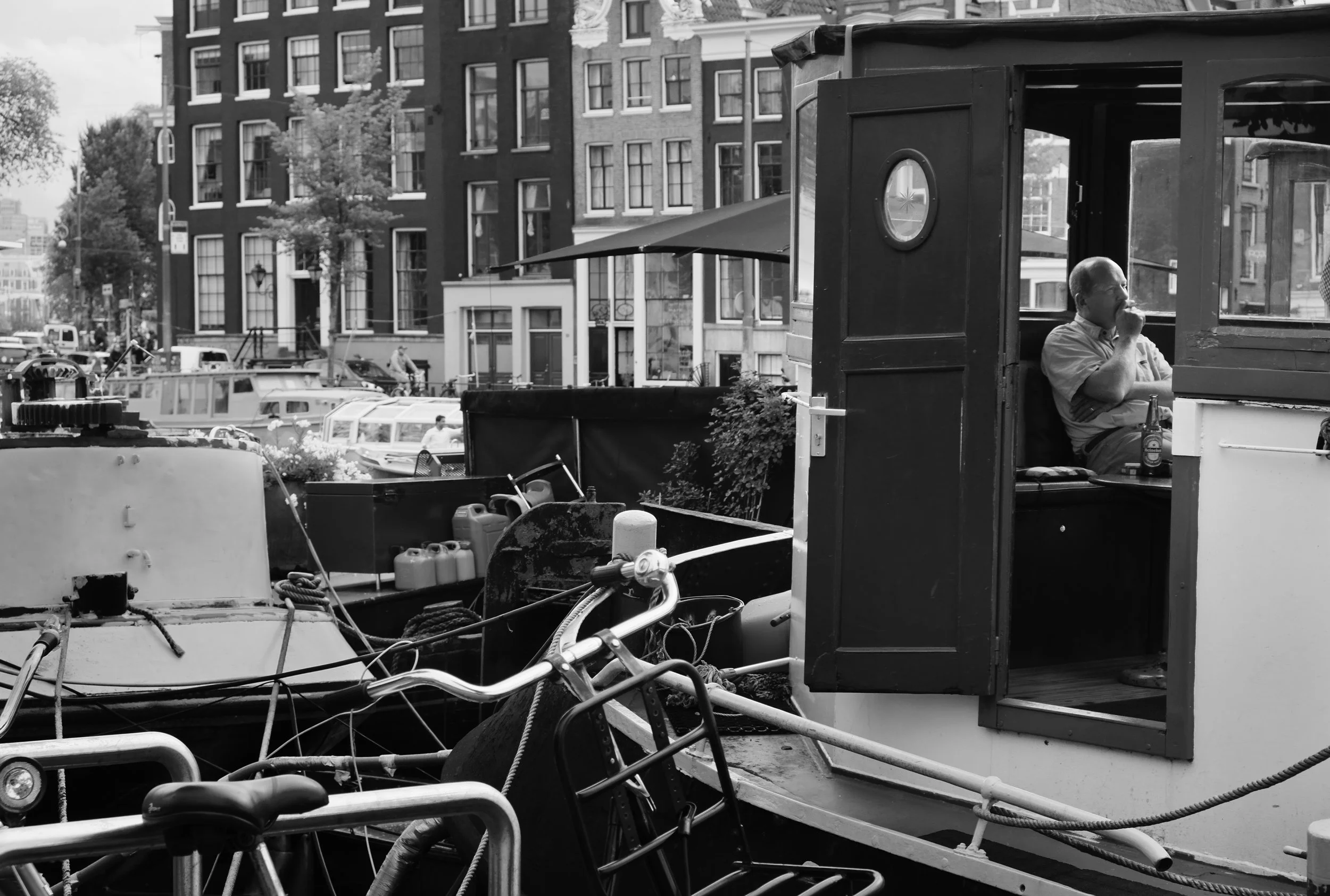 Black and white photograph of a man sitting inside a canal boat in Amsterdam