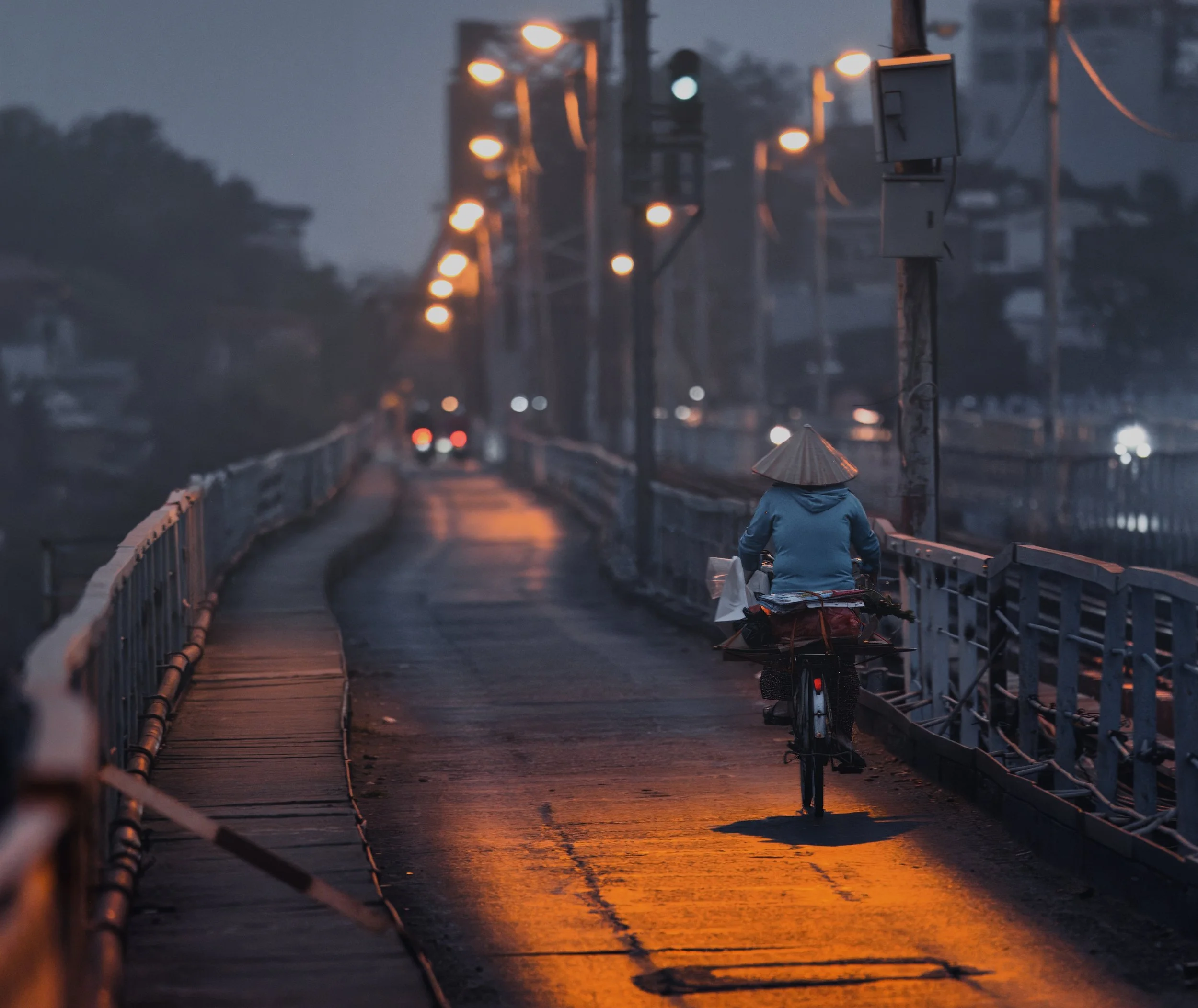Cyclist crossing Long Bien Bridge at dawn beneath glowing street lights