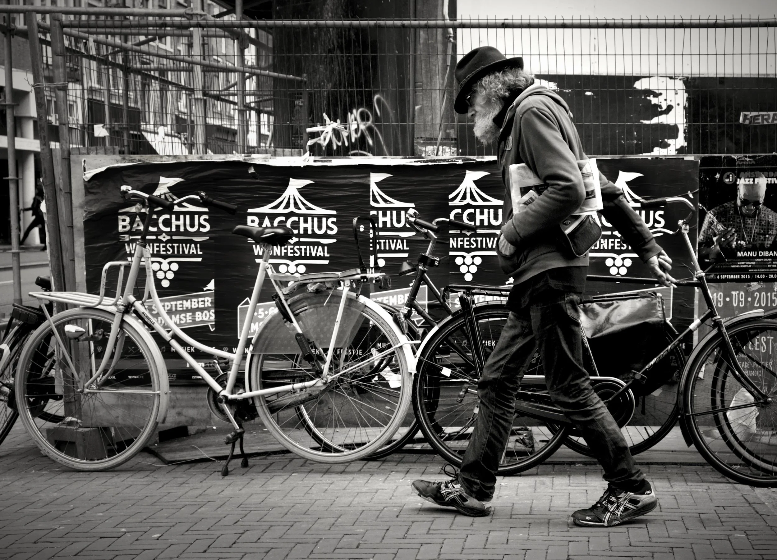 Black and white street photograph of a bearded man walking past bicycles in Amsterdam