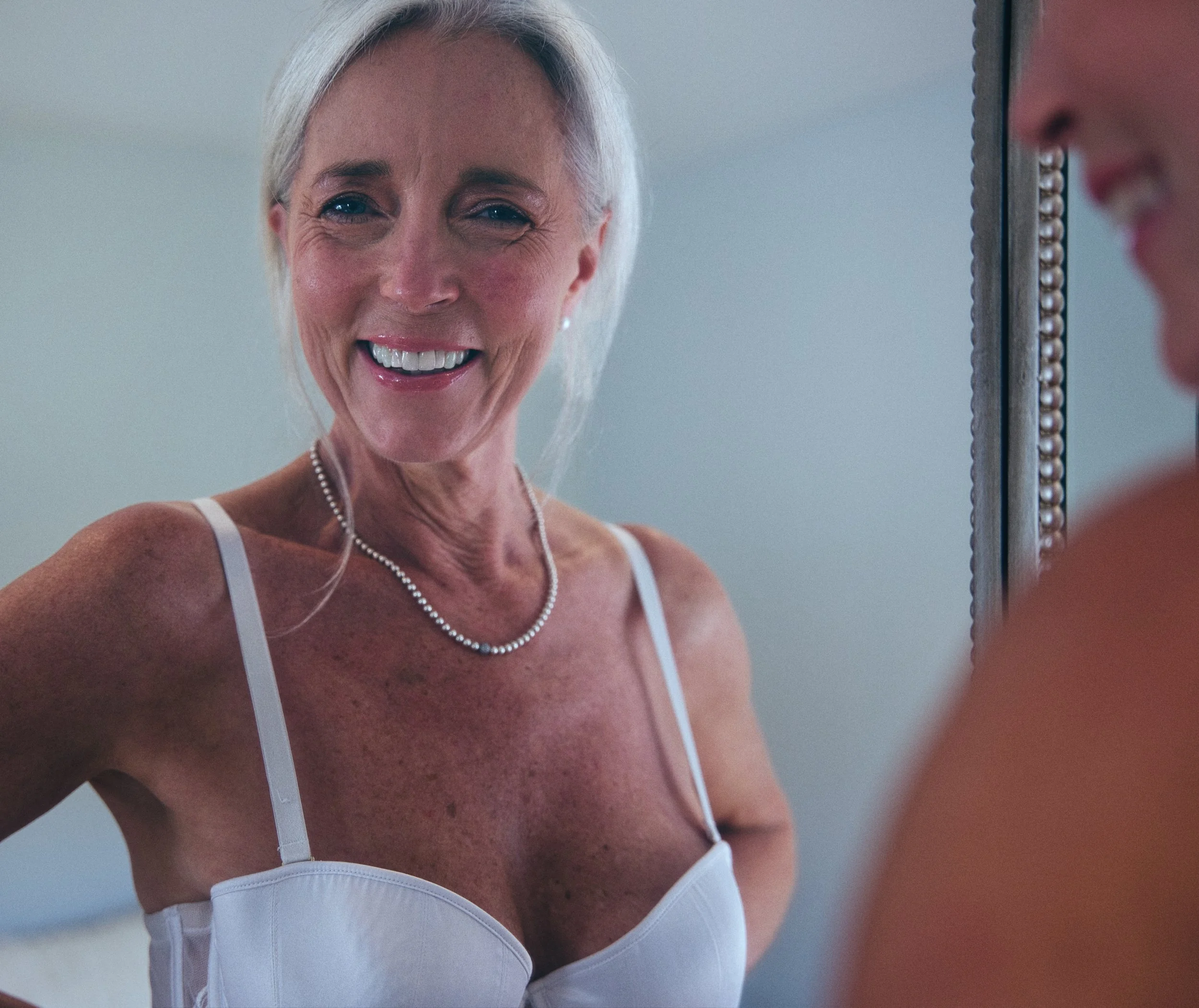 Portrait of a smiling woman reflected in a mirror wearing white lingerie