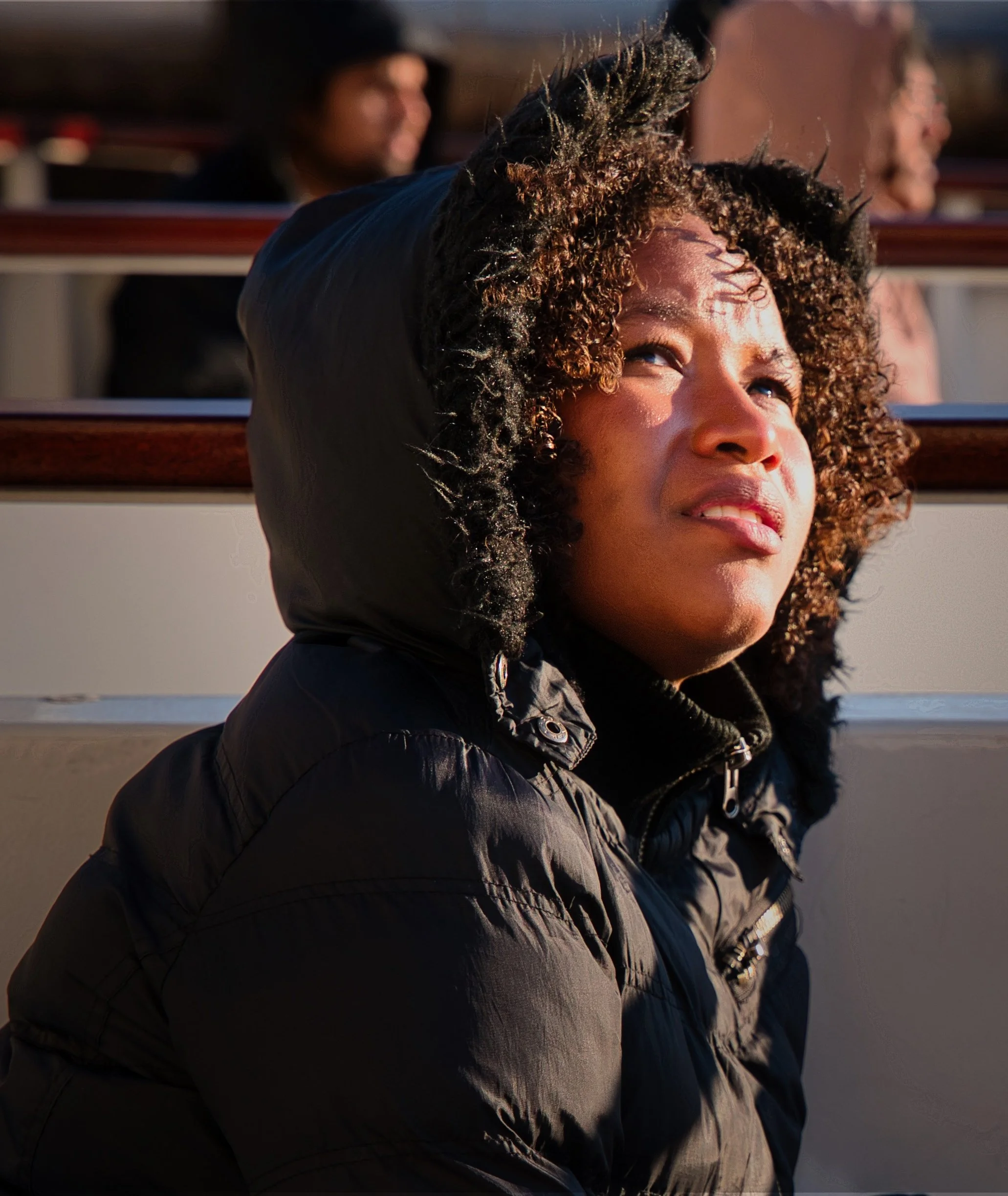 Young woman in a black hooded coat looking upward in warm evening light while seated on a boat in Chicago