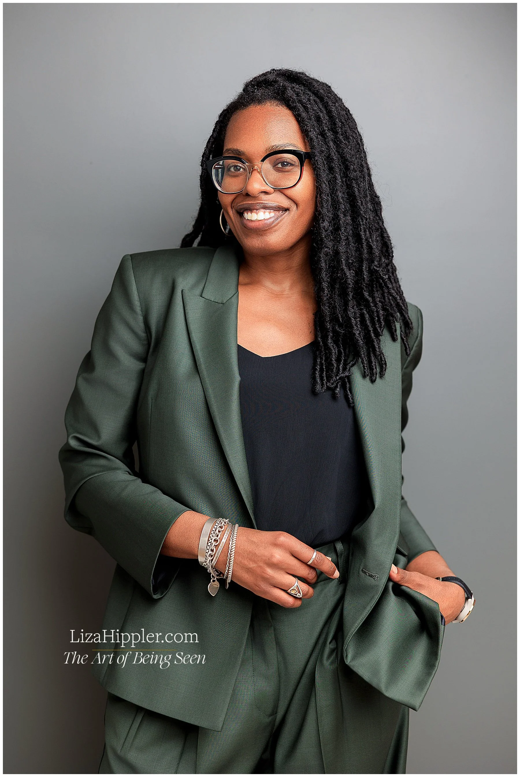 Professional brand photo of a black woman lawyer with dreads on a grey background wearing a green suit and a black shirt. Nashville photographer Liza Hippler.