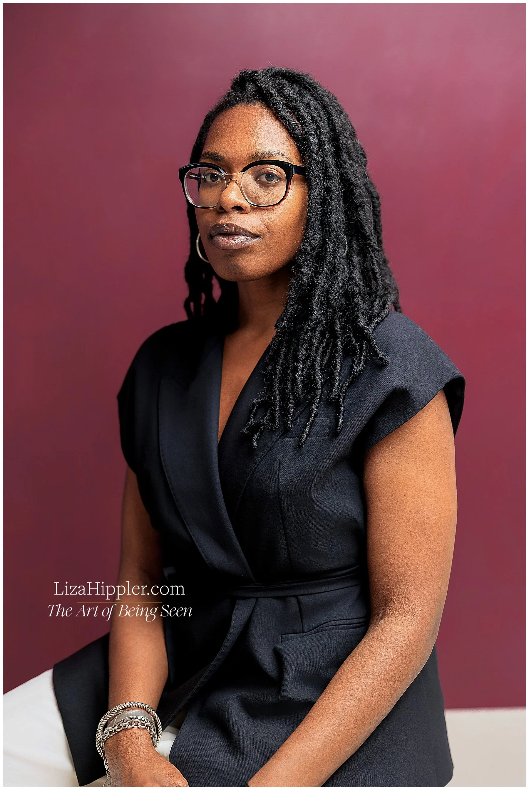 Professional brand portrait of a black woman lawyer wearing a black sleeveless top with a burgundy background