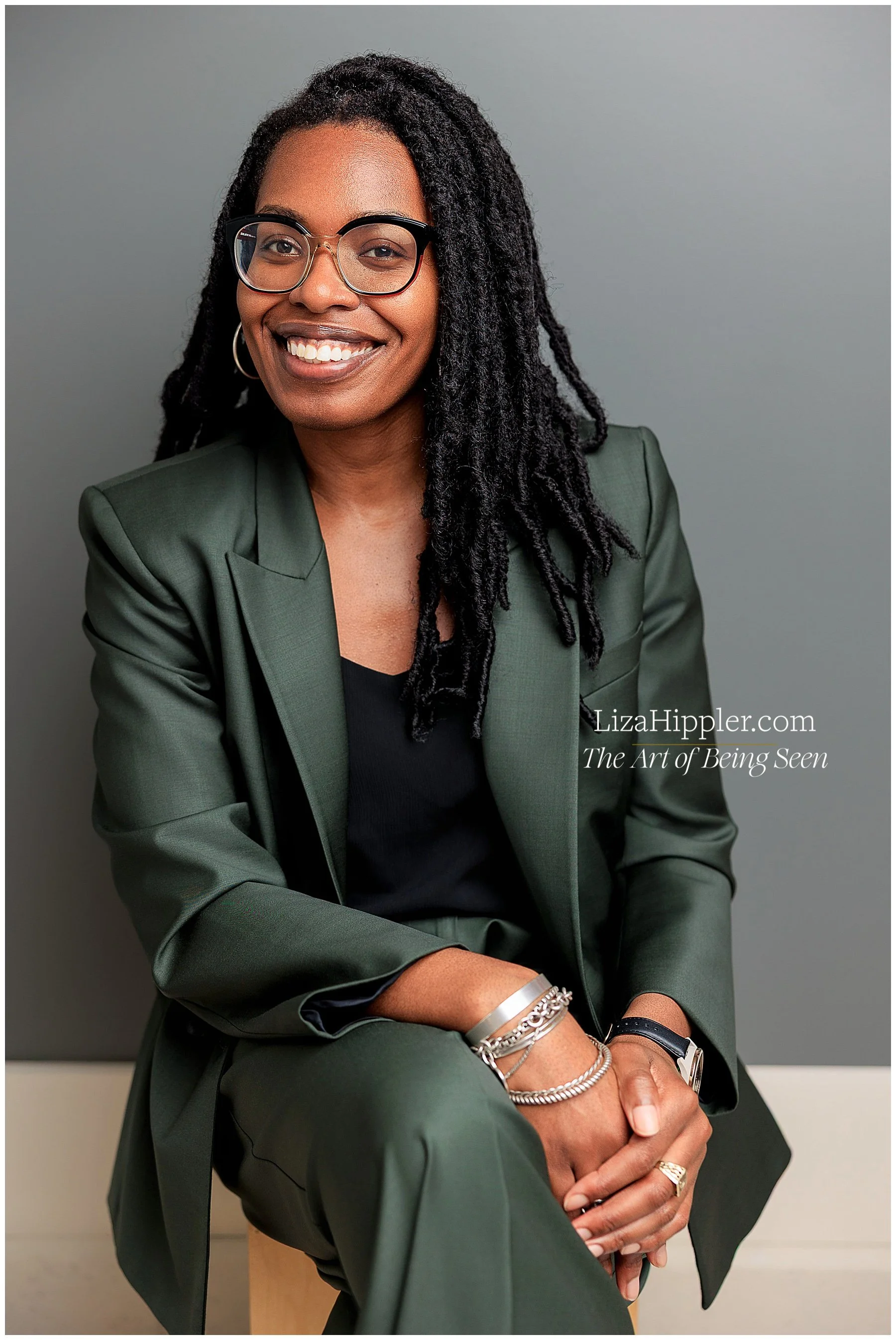 Professional headshot of smiling black woman lawyer in a dark green suit on a grey background.
