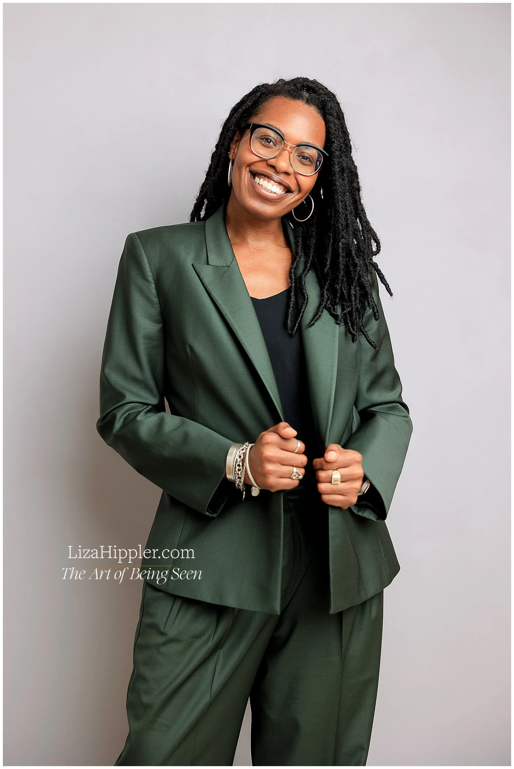 Professional photo of black female lawyer wearing a dark green shiny suit on a lavender background.