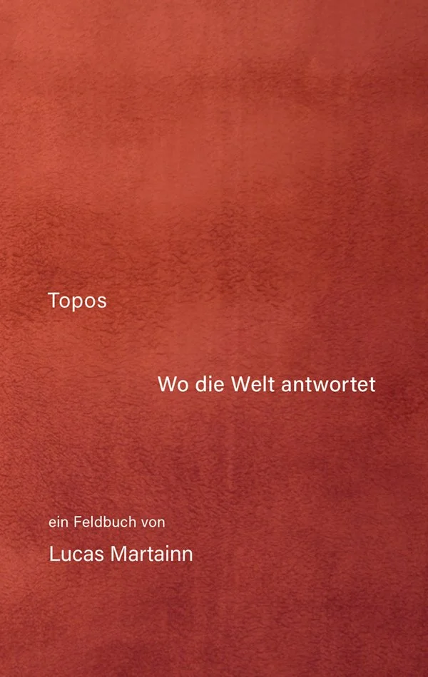 Buchdeckel mit roter, strukturierter Oberfläche, Titel 'Topos – Wo die Welt antwortet', und Autor 'Lucas Martainn'. Beschreibung: Ein Feldbuch.
