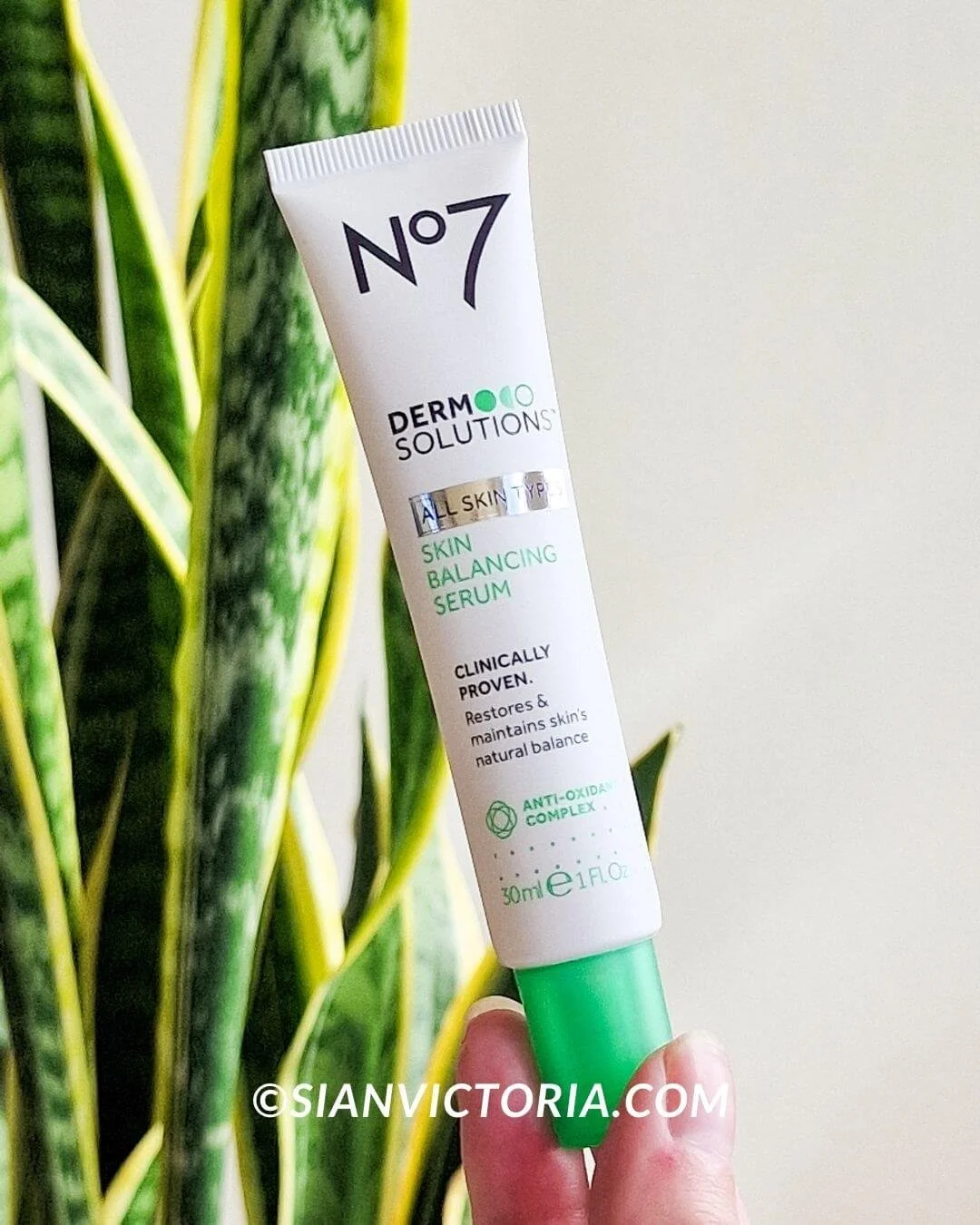 a hand holding a no7 skincare serum with a snake plant in the background