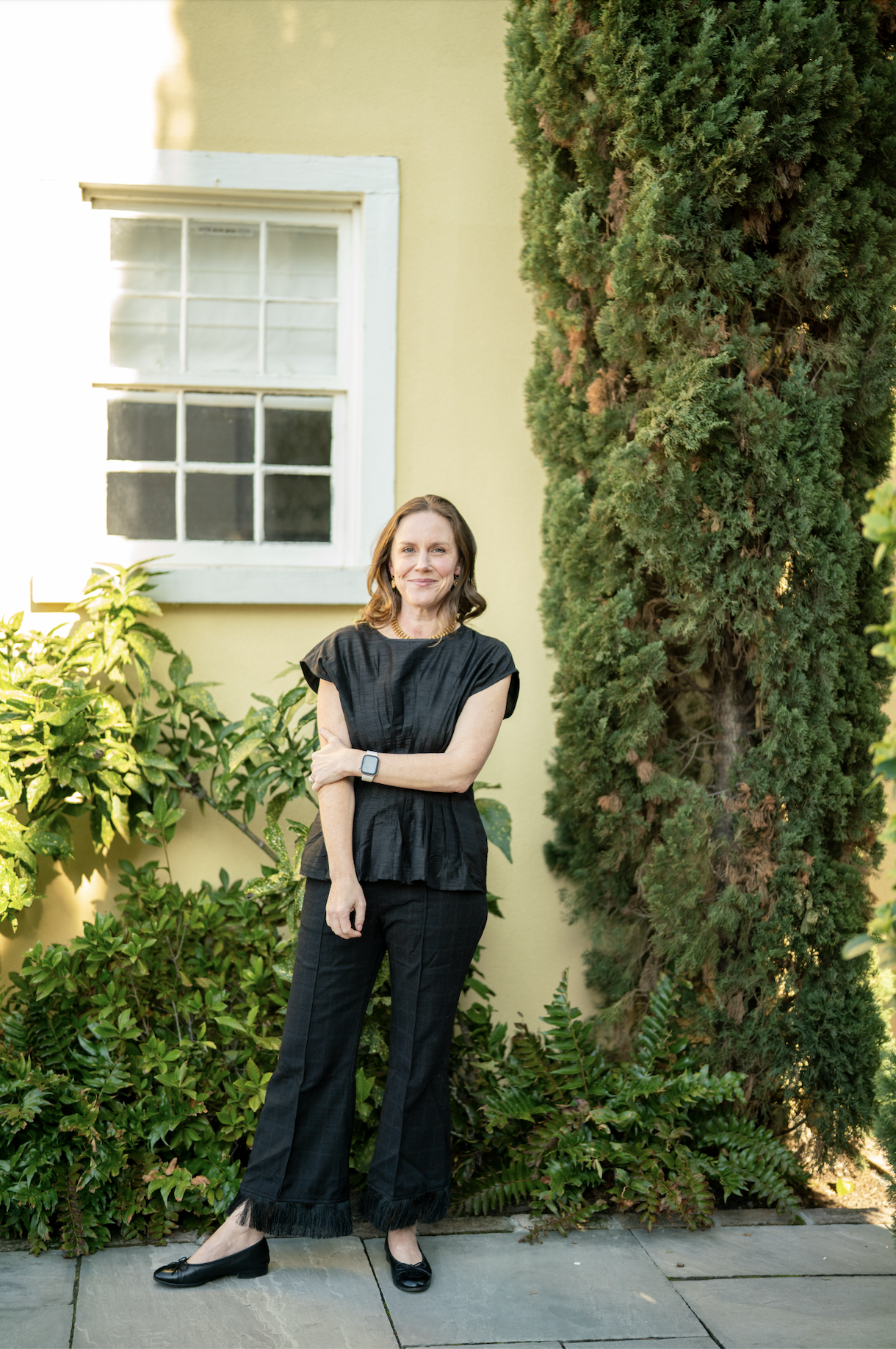 A woman with blonde hair, wearing a black puff-sleeve dress and a gold necklace, smiling in a kitchen.