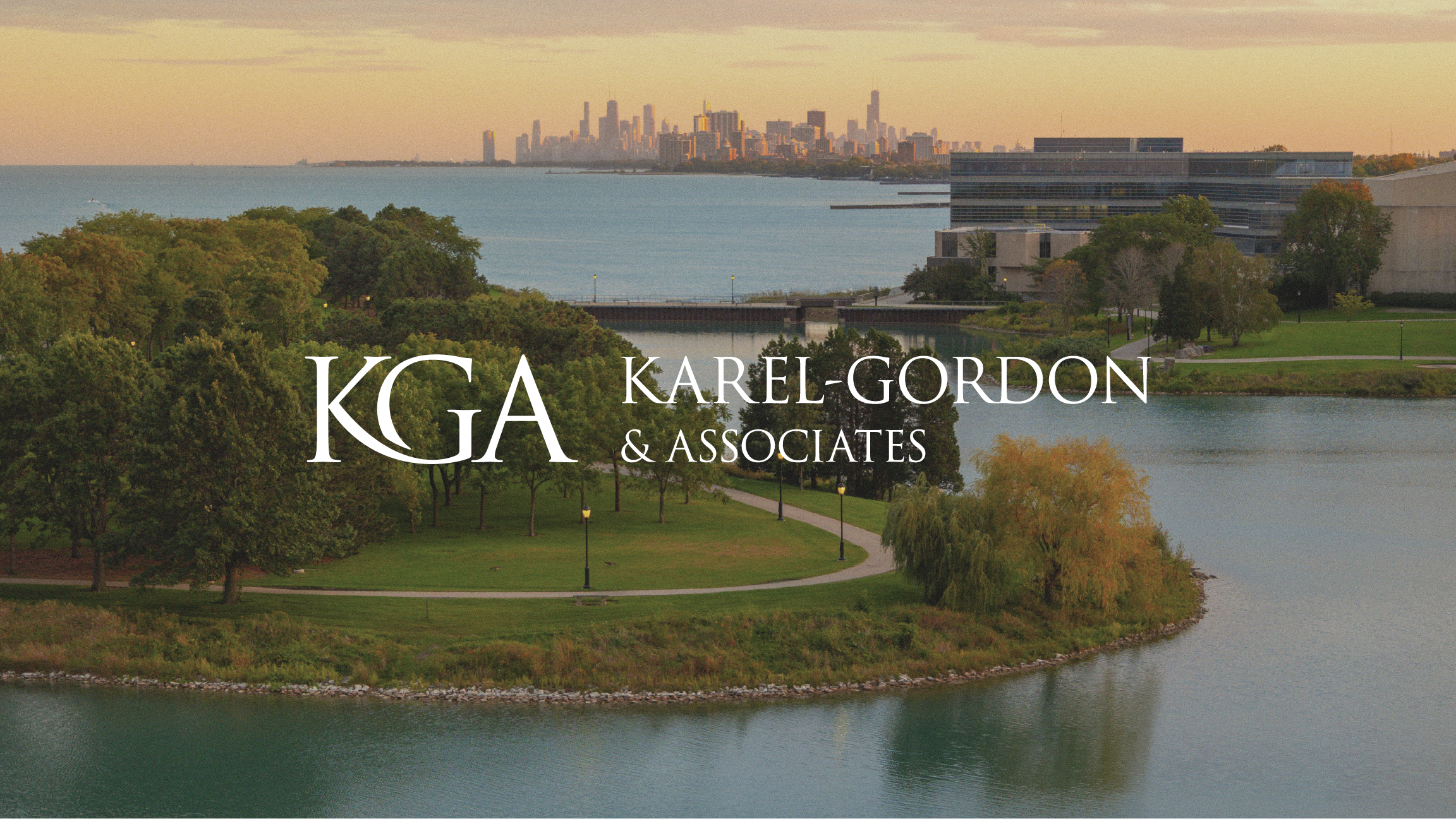 A scenic view of a park with trees and a small body of water, overlooking a city skyline in the distance during sunset. The image features the logo and name of Karel-Gordon & Associates, with the text ''KGA'' and ''Karel-Gordon & Associates''