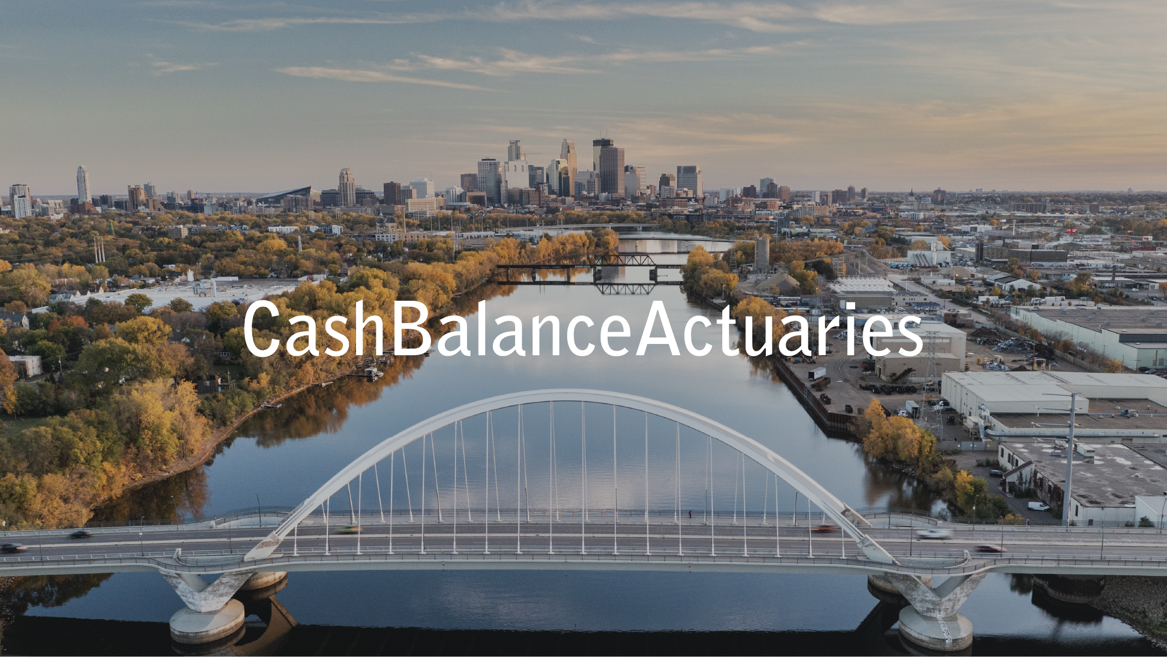 Aerial view of a city skyline with a river in the foreground, featuring a modern white arch bridge and autumn trees, with the words 'CashBalanceActuaries' overlayed.