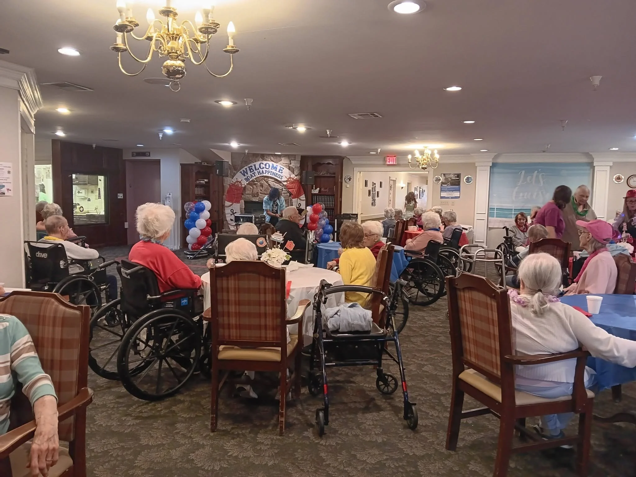 Senior citizens gathered in a cozy room with a nautical-themed decoration, balloons, and tables, attending a social event or celebration.