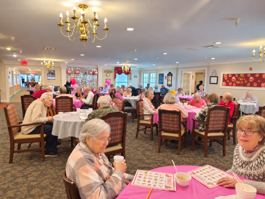 Senior citizens dining at a decorated event space with tables, chairs, and holiday decorations.