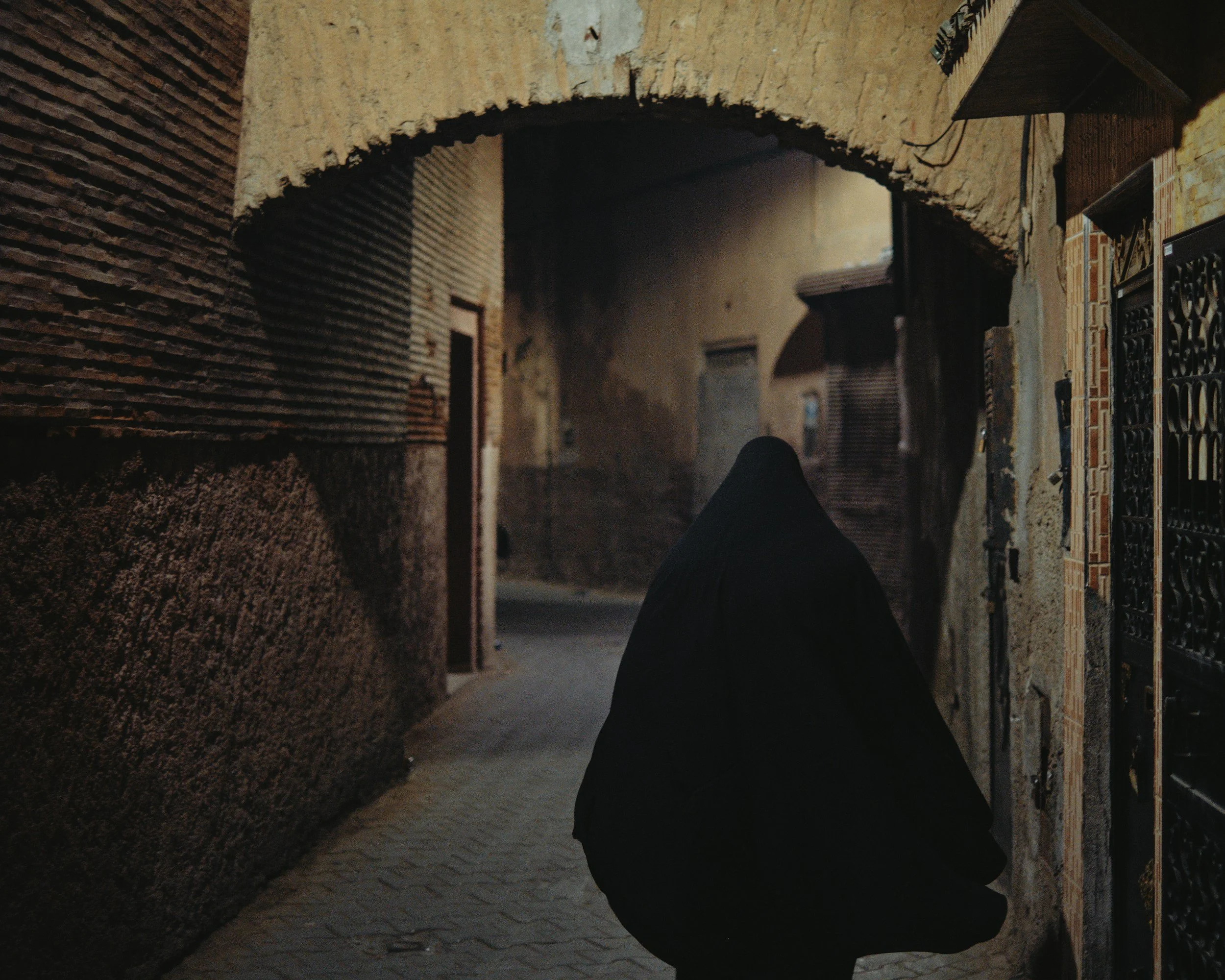 Cloaked figure walking through alley