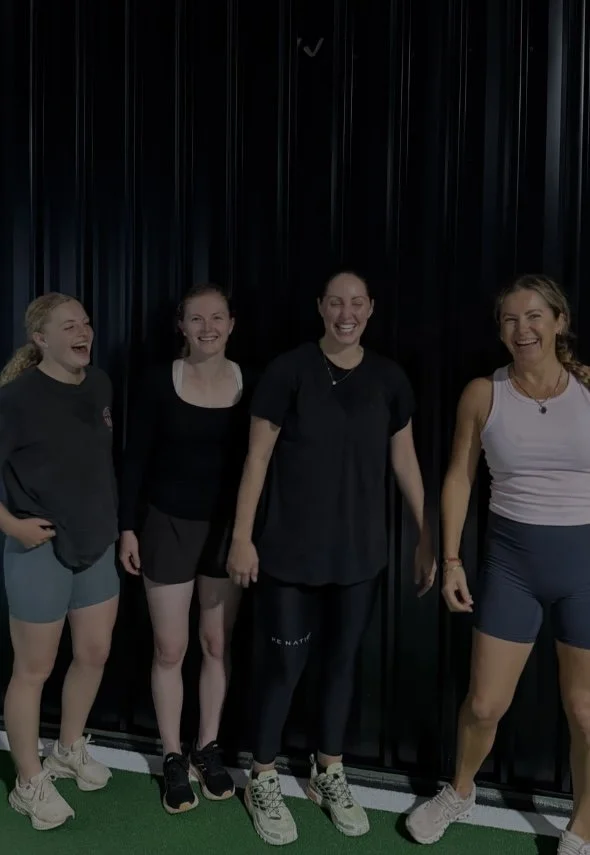 Four women standing together indoors against a black curtain, smiling and laughing.