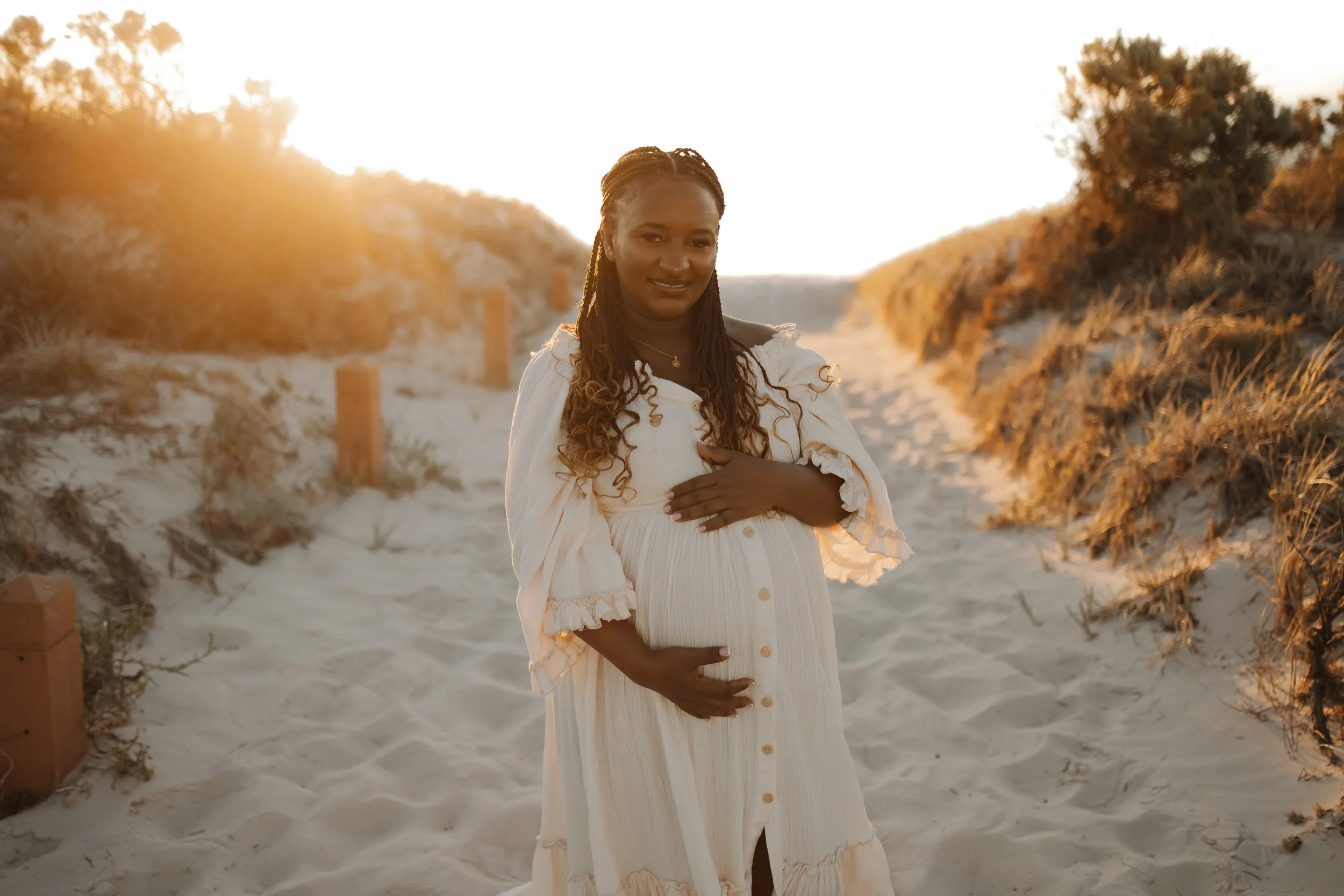 beautiful pregnant African women standing in the middle of a sandy pathway that leads to Tennyson beach (west of Adelaide). She wears a flowy dress that is included in Dannielle Cook Photography's Client closet