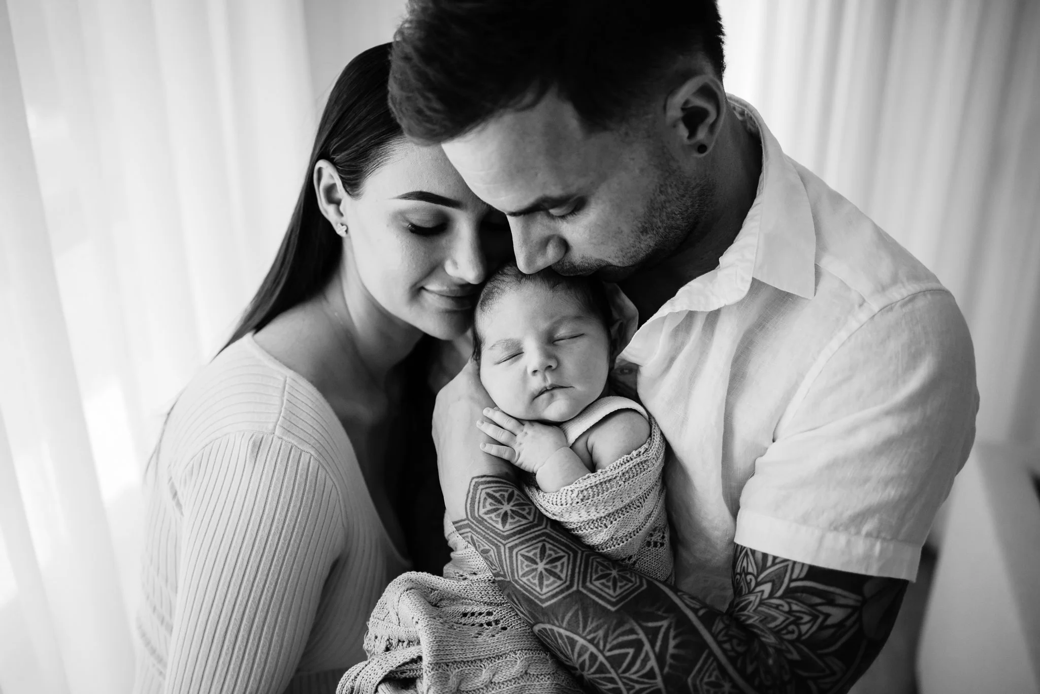 Adelaide Dad holds his newborn baby girl while kissing her head as new mum closes her eyes and leans into them both.