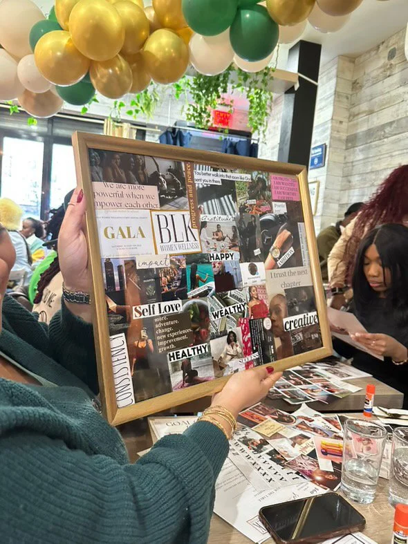 Person holding a collage board with words and images at a social event, decorated with gold, white, and green balloons hanging from the ceiling.