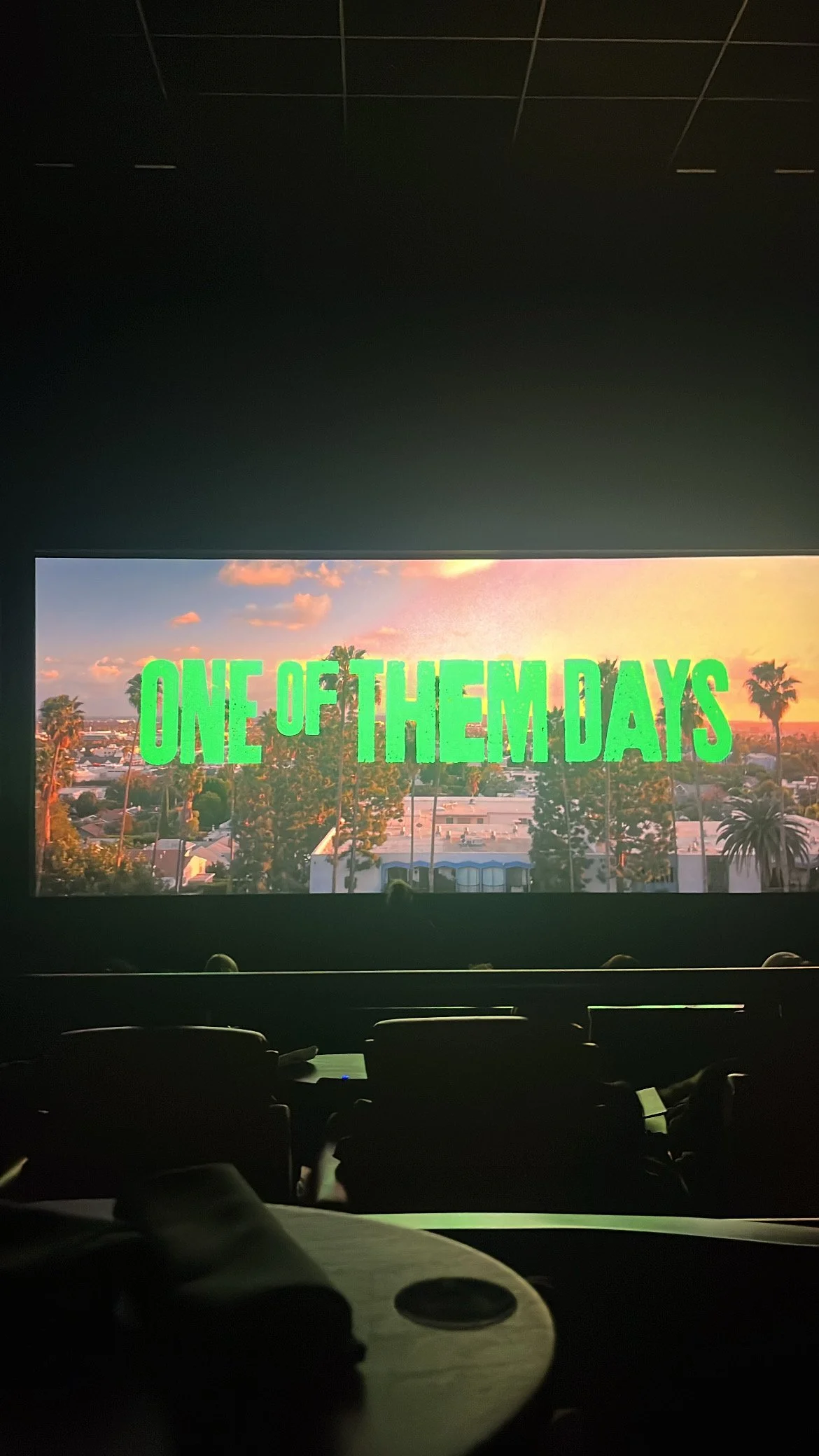 A movie theater screen displays the title "One of Them Days" against a sunset background with palm trees and buildings.