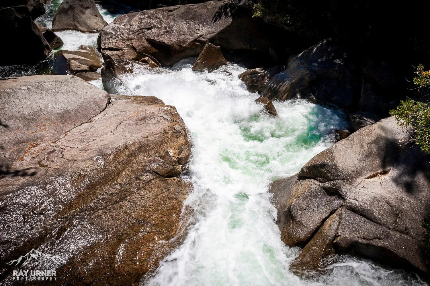 Rushing mountain stream flowing over and between large, smooth rocks in a rocky riverbed.