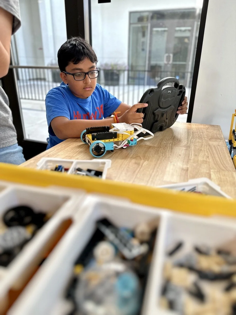 A student working on an iPad to program a LEGO robotics project, surrounded by LEGO Technic and Mindstorms parts for the FIRST LEGO League Challenge.