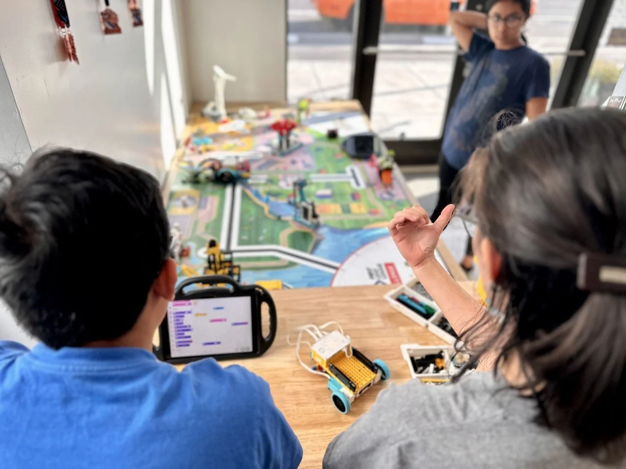 A robotics coach discussing the programming of a FIRST Tech Challenge robot with two engaged students, reviewing autonomous and teleoperated functions.