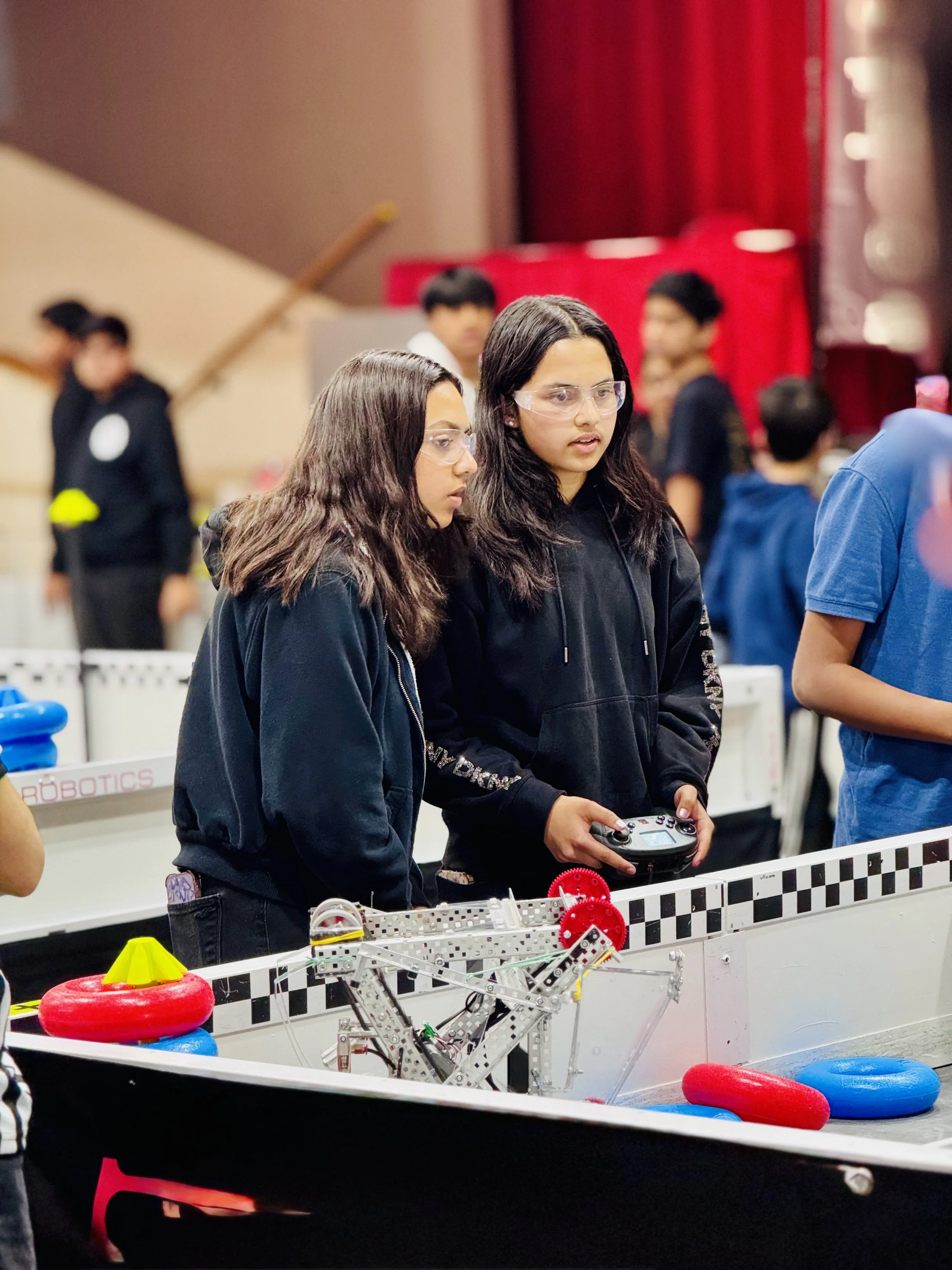 Two girls controlling their robot during an intense VEX robotics match on the competition field.