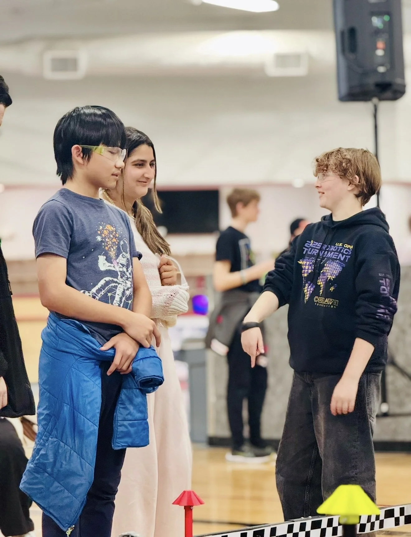 Three students at a robotics competition smiling and discussing their game strategy.