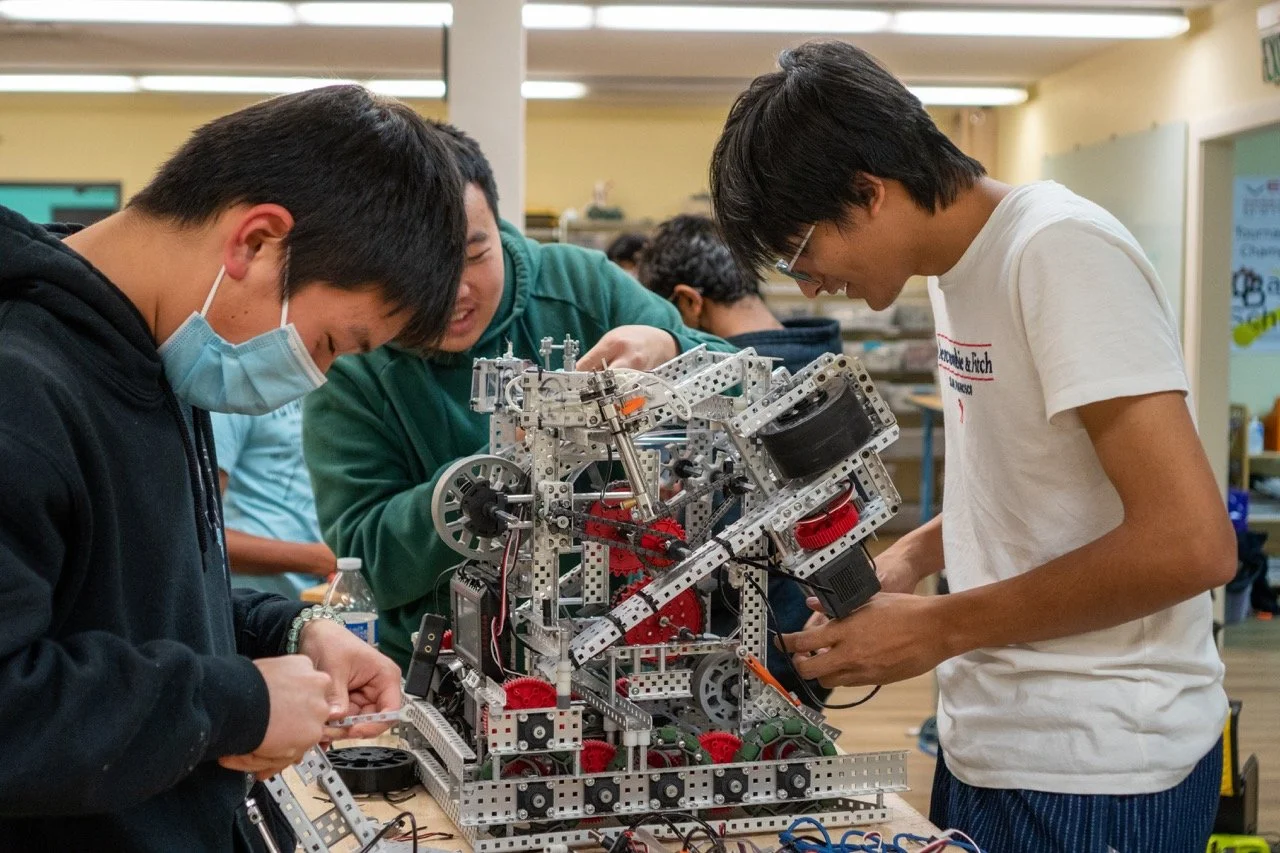 A team of three students collaborating on assembling their VEX robot for an upcoming robotics challenge.