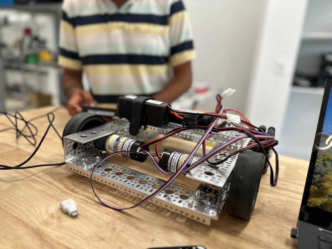 A close-up view of a FIRST Tech Challenge robot's drivetrain, with a student working in the background, ensuring precision in movement.