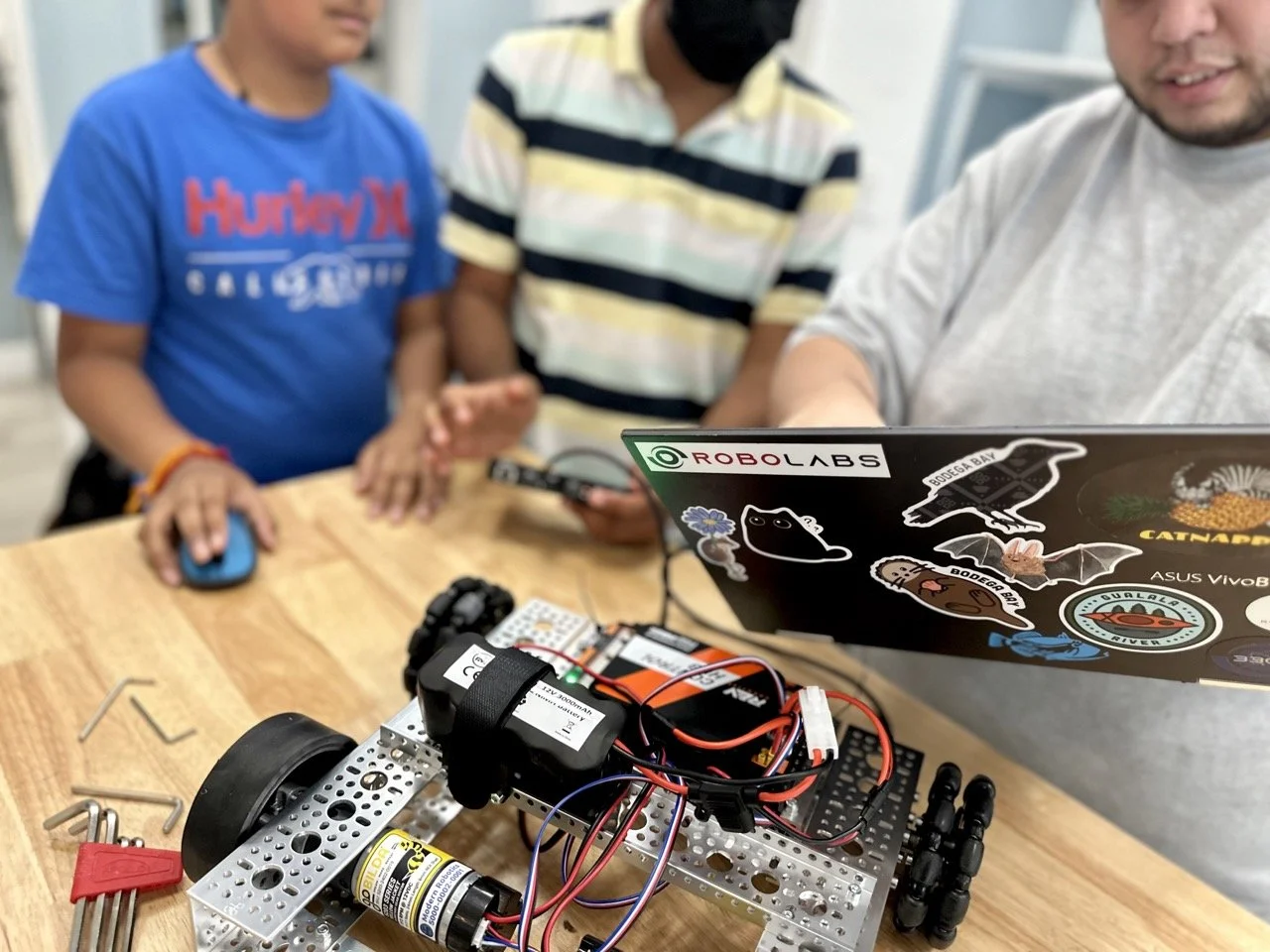 A dedicated coach walking two highly focused students through the coding logic of their FIRST Tech Challenge robot, refining their automation strategies.