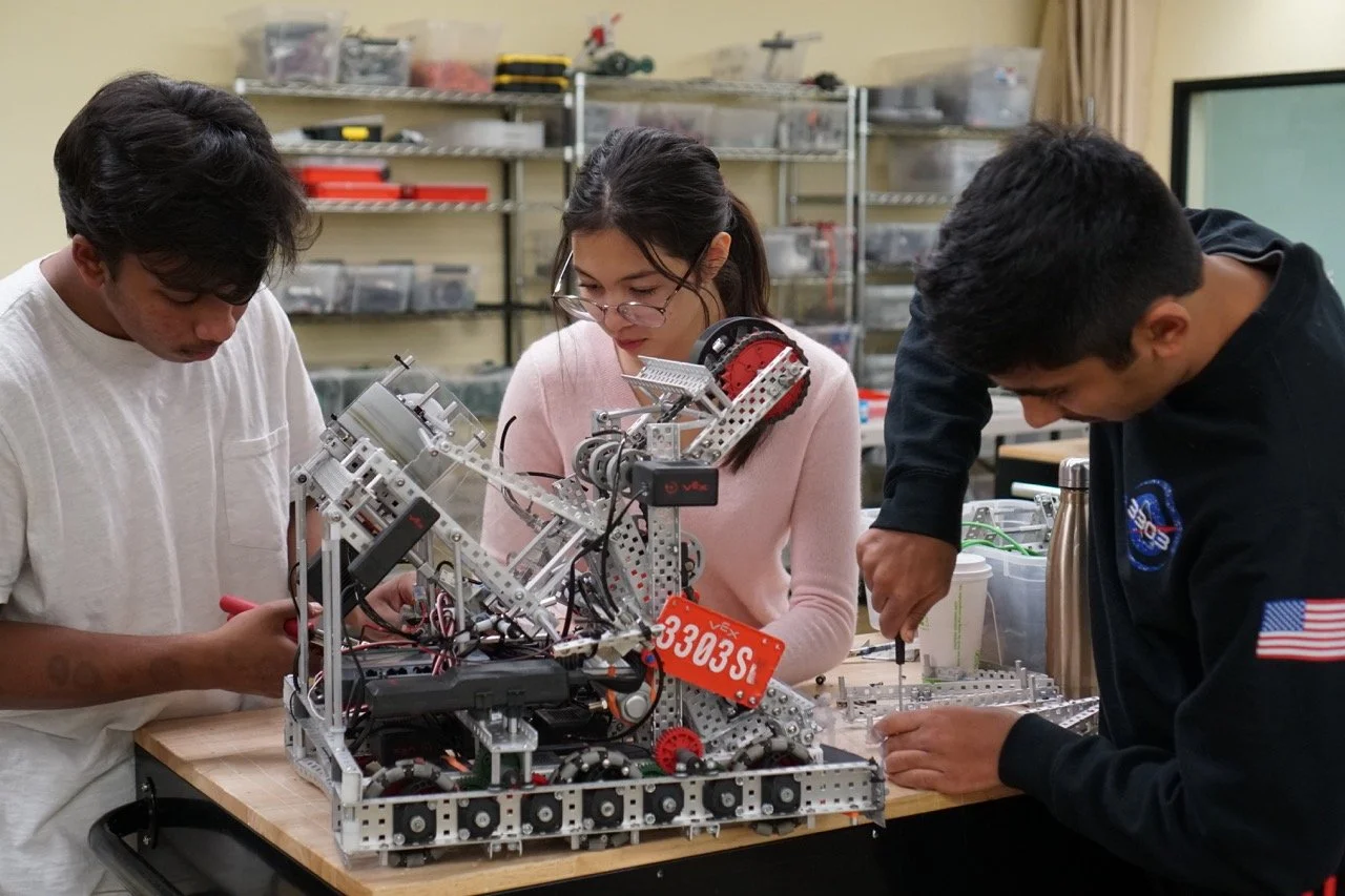 A team of three students intensely focused on assembling and programming their VEX robot for an upcoming robotics challenge.