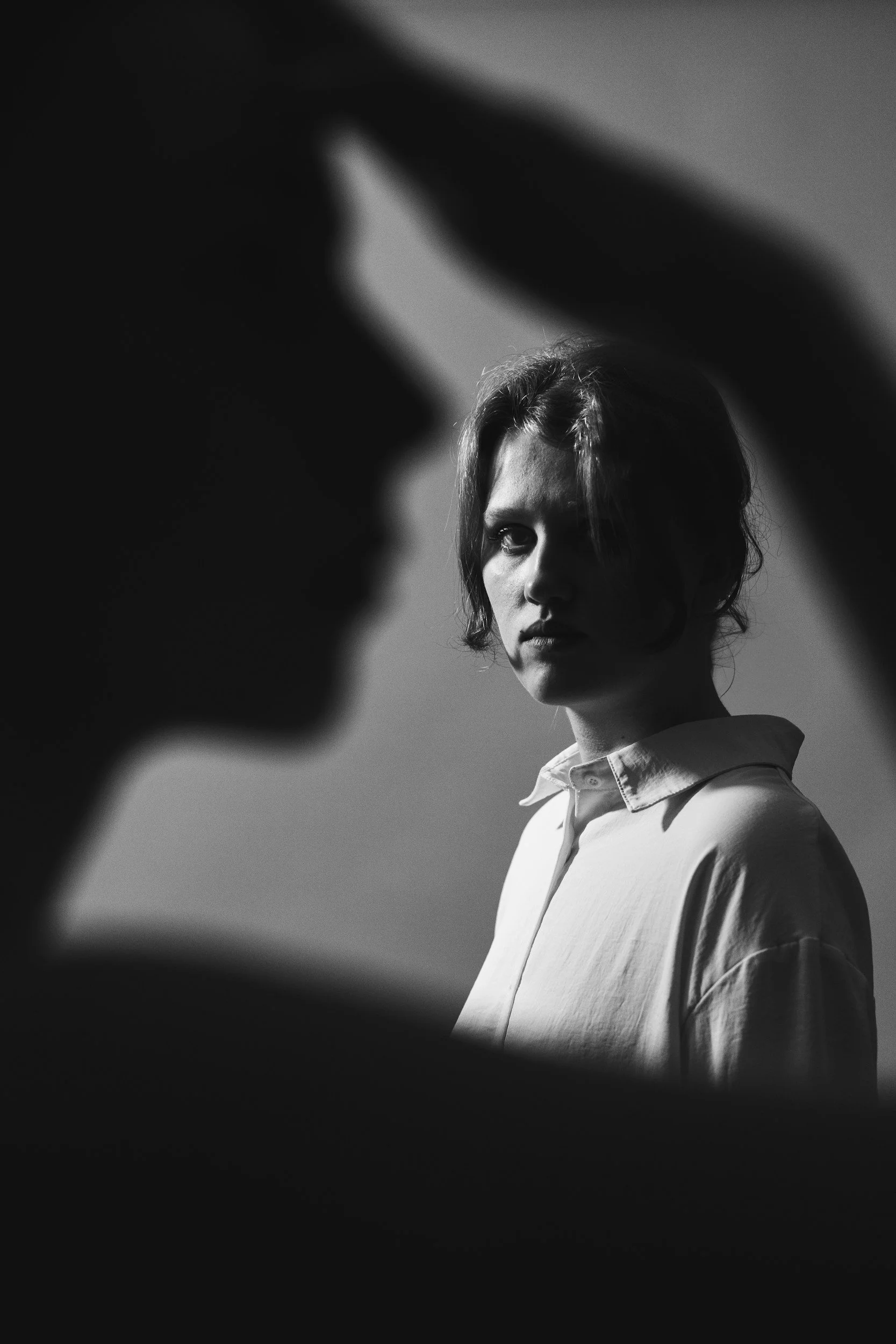 A woman in silhouette is unaware as a man stares at her from a distance, suggesting danger and unease.