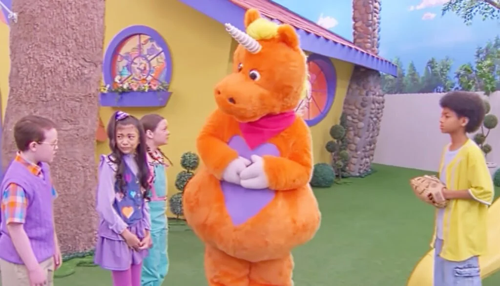 A screenshot from the film Buddy (2026) featuring the title character, Buddy and a group of kids in a colorful outdoor environment