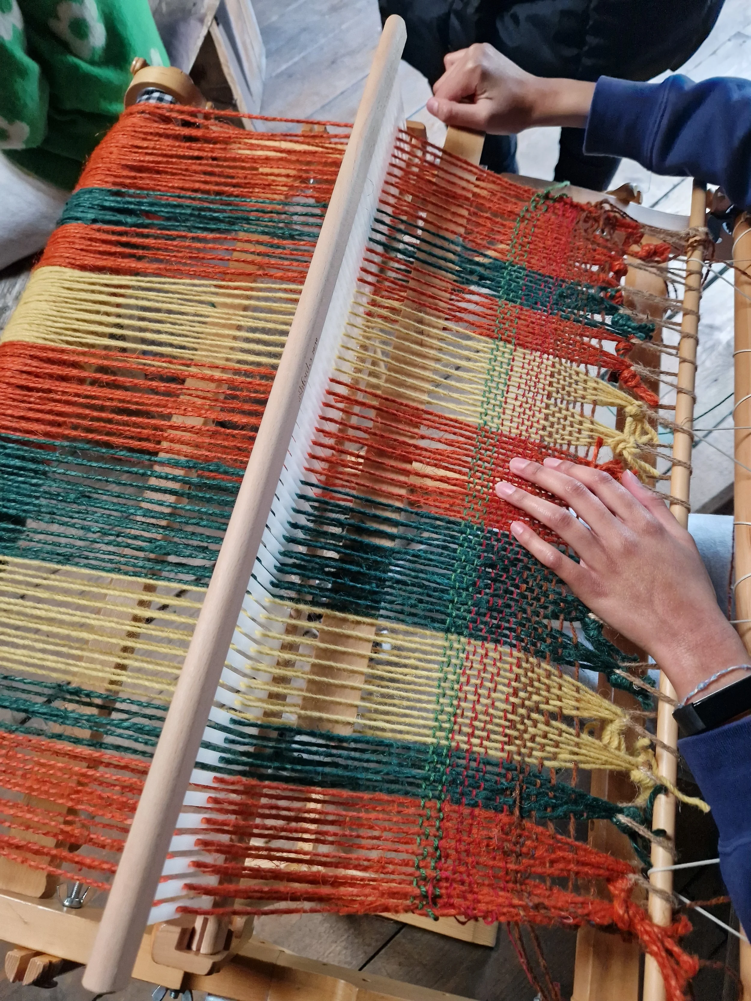 Yarn is on a loom and hands prepare to weave