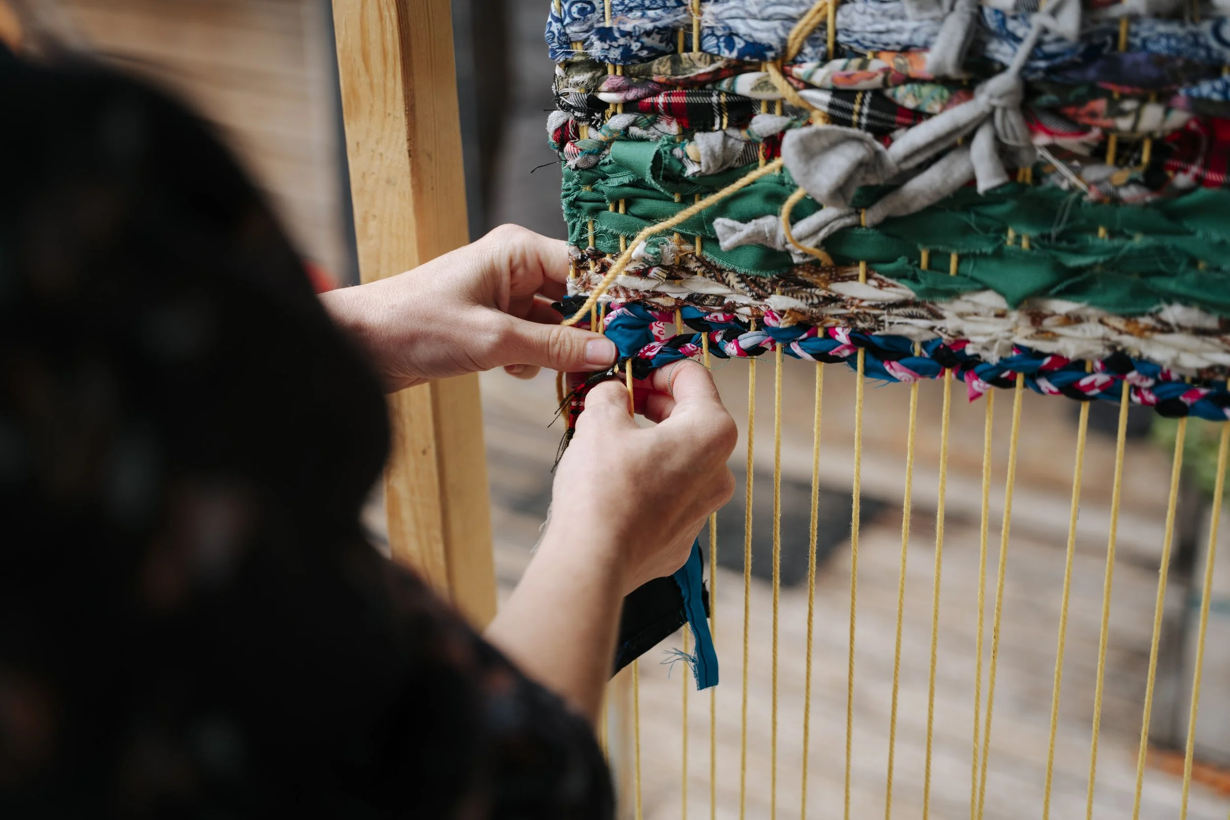 A person weaves textiles onto an upright loom
