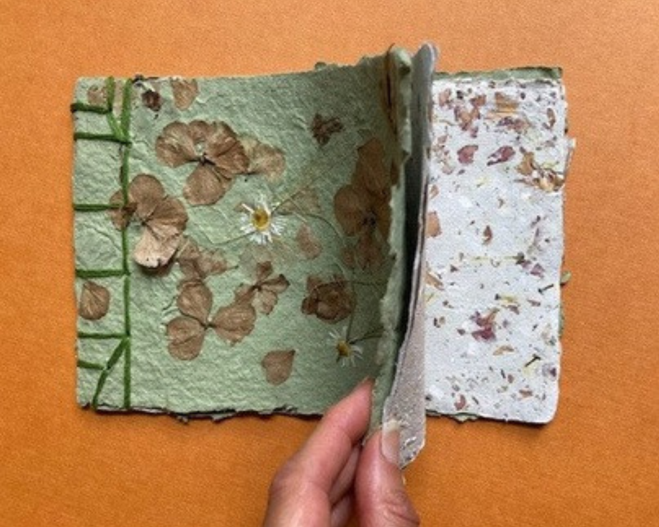 a hand flips the front page of a handmade paper book