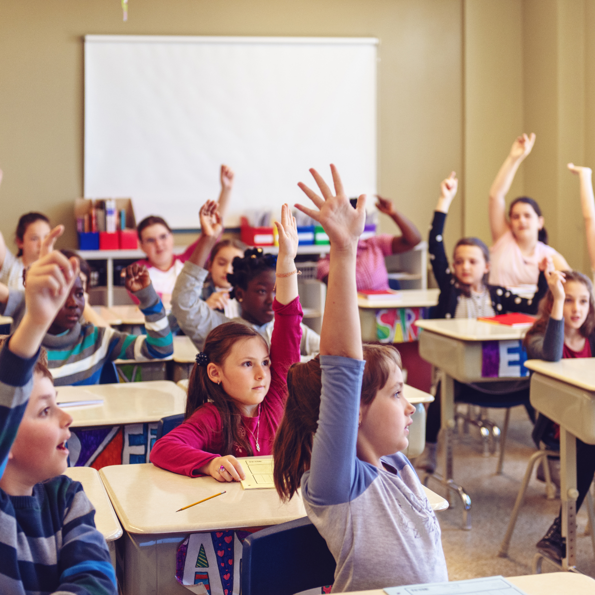 Elementary school classroom with students raising their hands during a lesson.