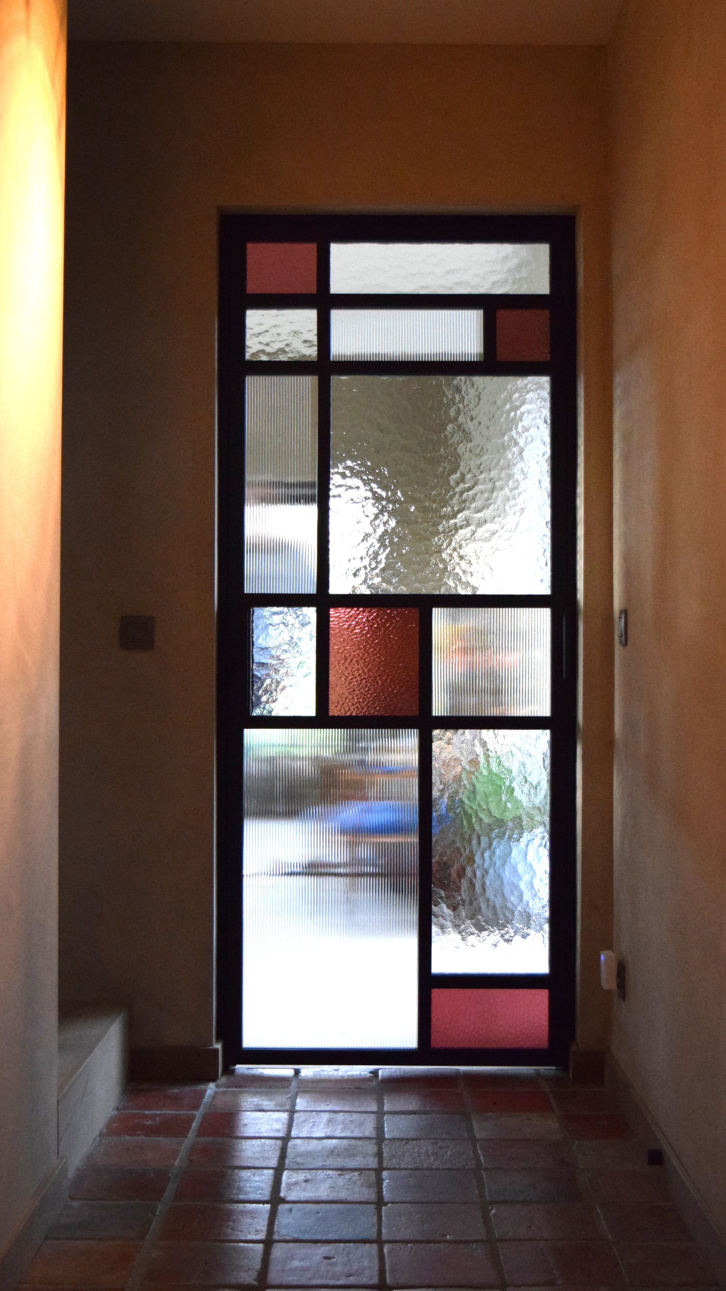 Stalen scharnierdeur met atypische onderverdeling, verschillende soorten glas waaronder raywall-, cathedraal- en gekleurd glas bevestigd met glaslatten, rolslot met handgreep