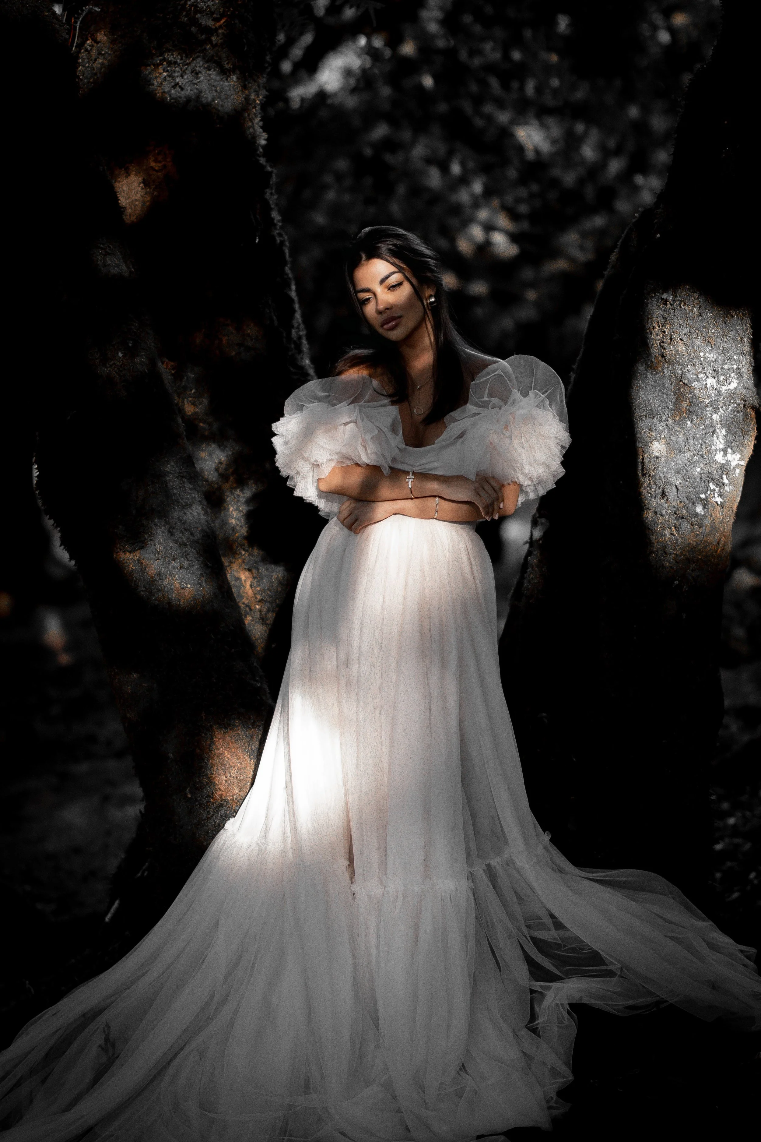 Woman in an elegant white ruffled gown posing inside a dark rocky cave