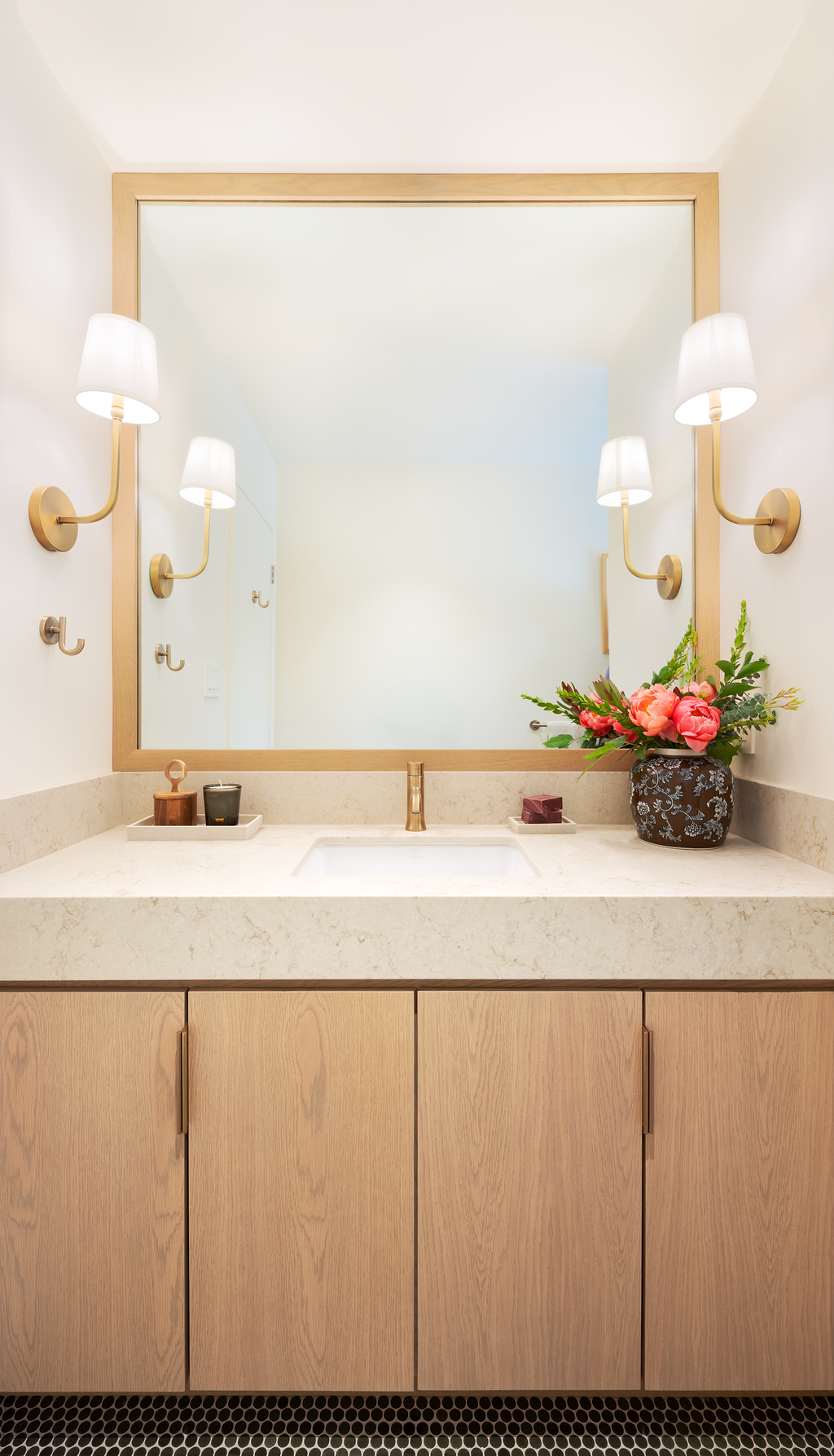 Bathroom vanity with oak cabinetry, marble counter, brass sconces, and black penny-tile floor in a Santa Rosa home by AVCO Design